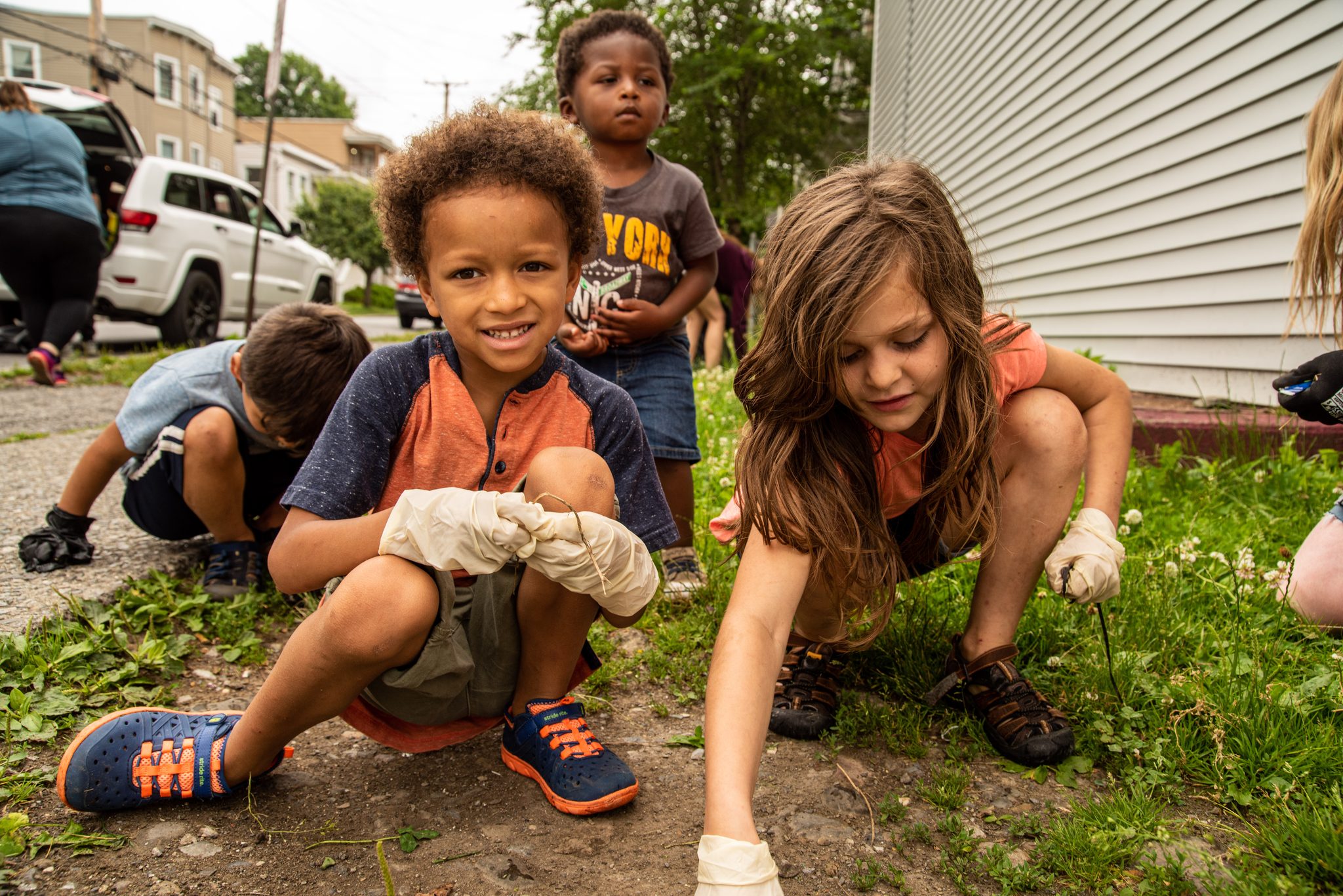 Gloved up and grinning, the youngest crew pulls weeds from the sidewalk cracks.