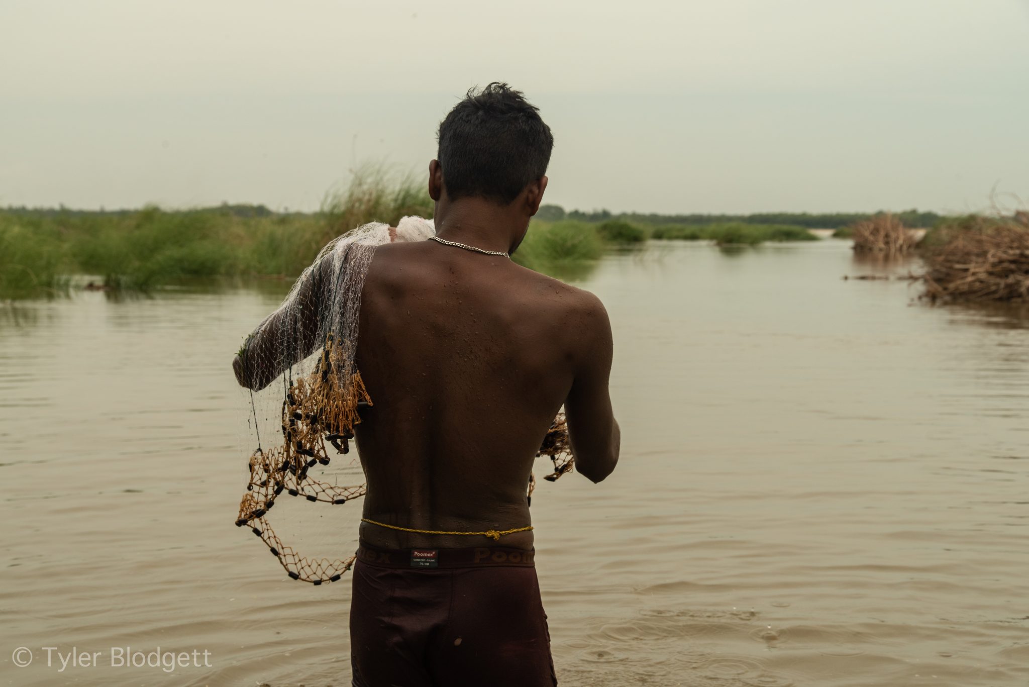 A fisherman wades out with his net over his shoulder.
