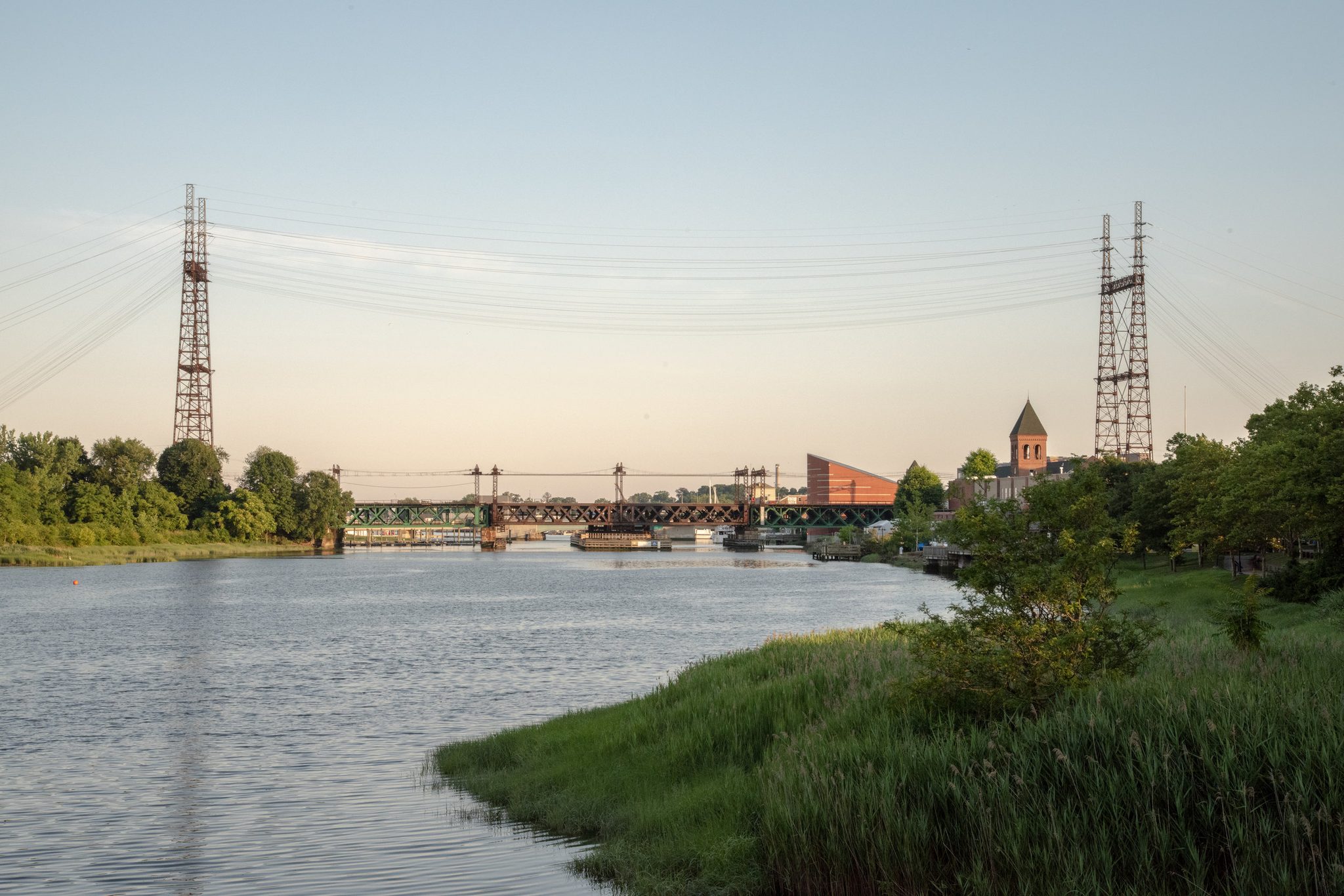 Power towers and an old railroad bridge span the river in the evening light.