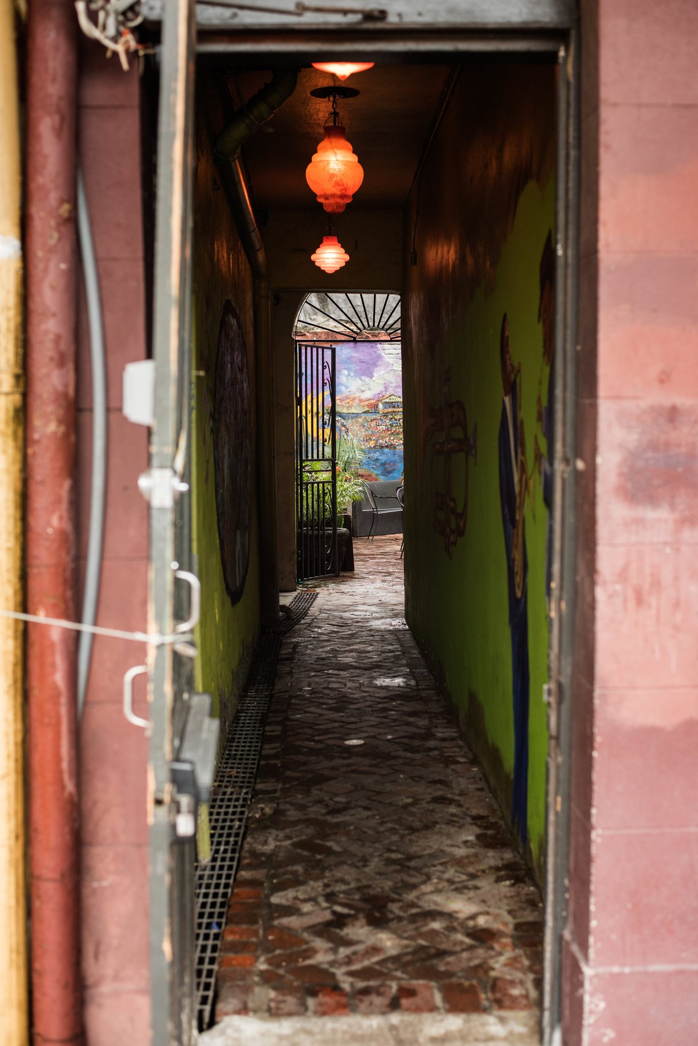 A narrow alley runs back under red lanterns, murals on both walls.