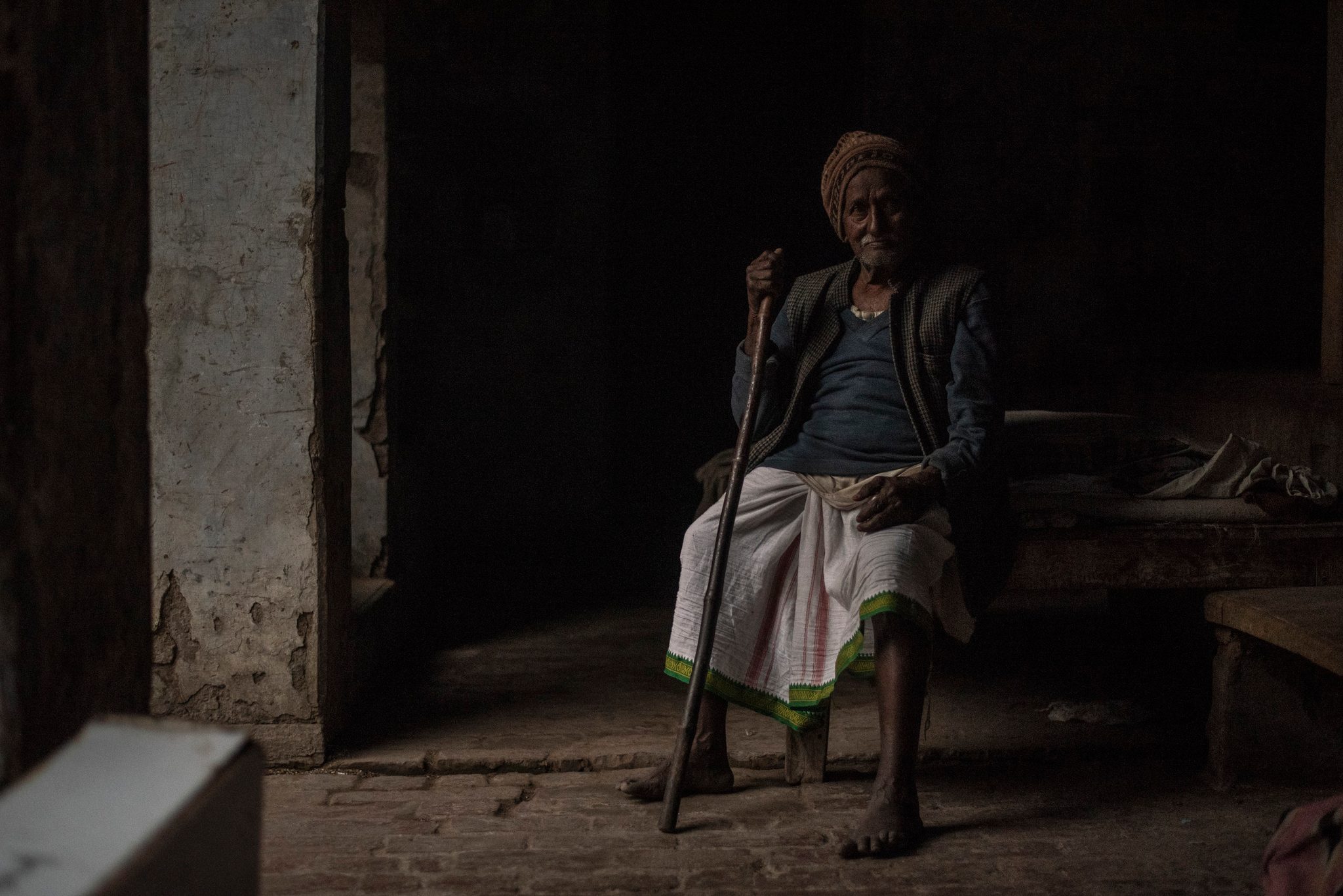 Man sits with staff in abandoned building where his family is residing during the mela.