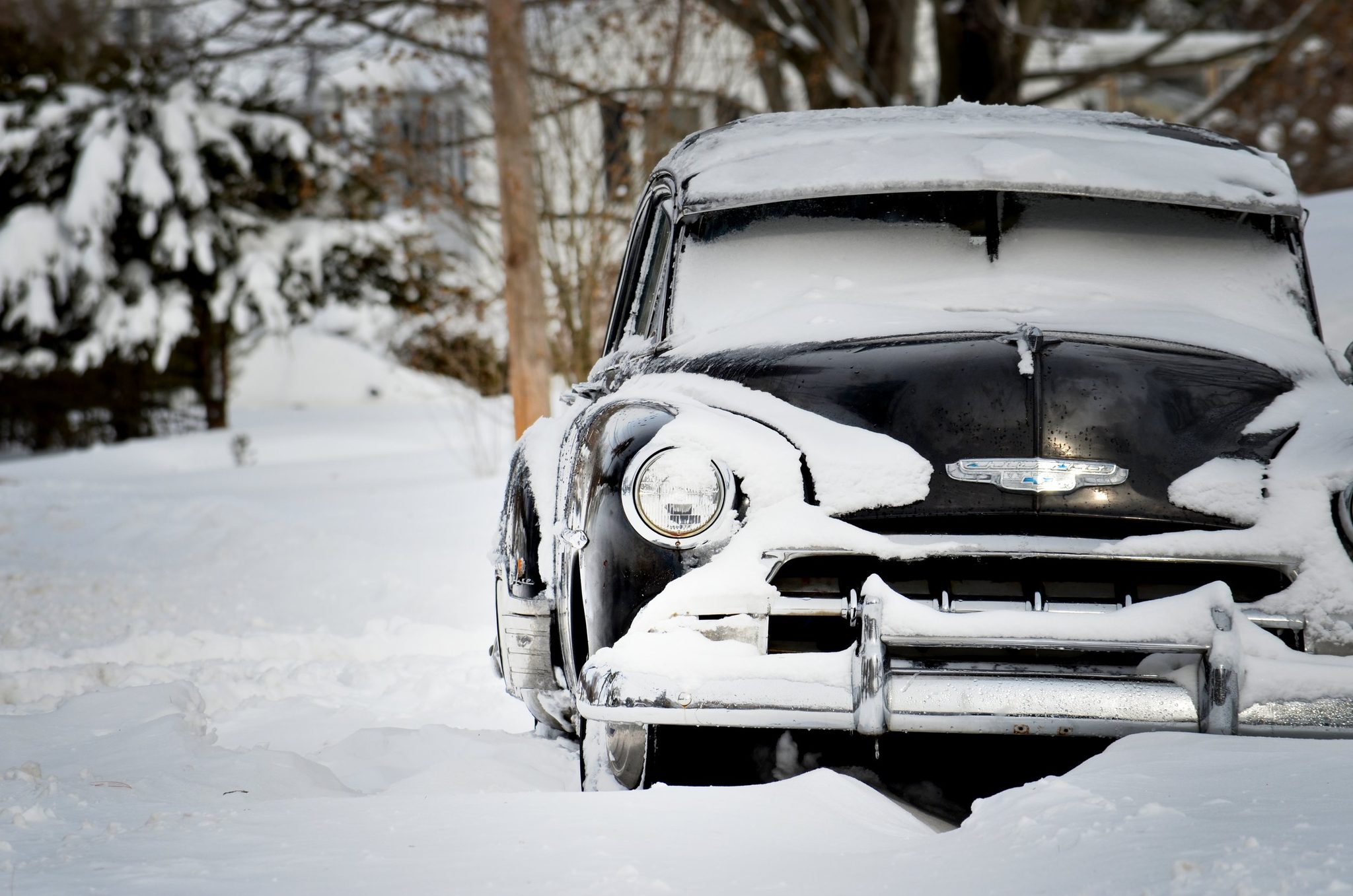 Snow piles high on the old car's hood, its grille still grinning through.