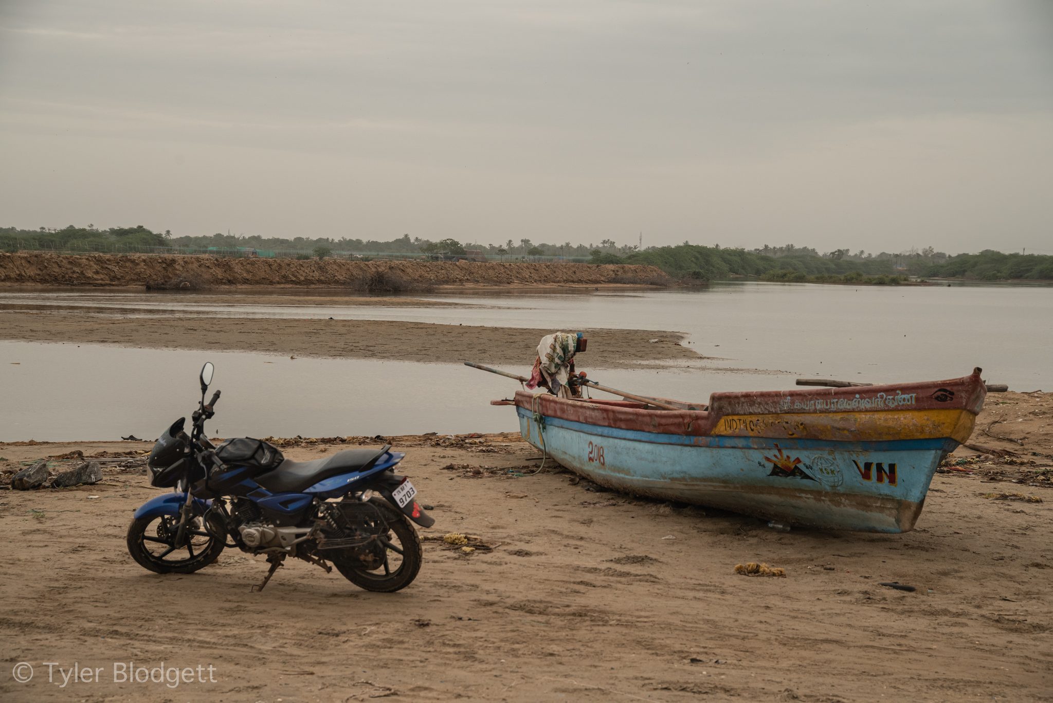 A motorbike waits beside a boat pulled up on the riverbank.