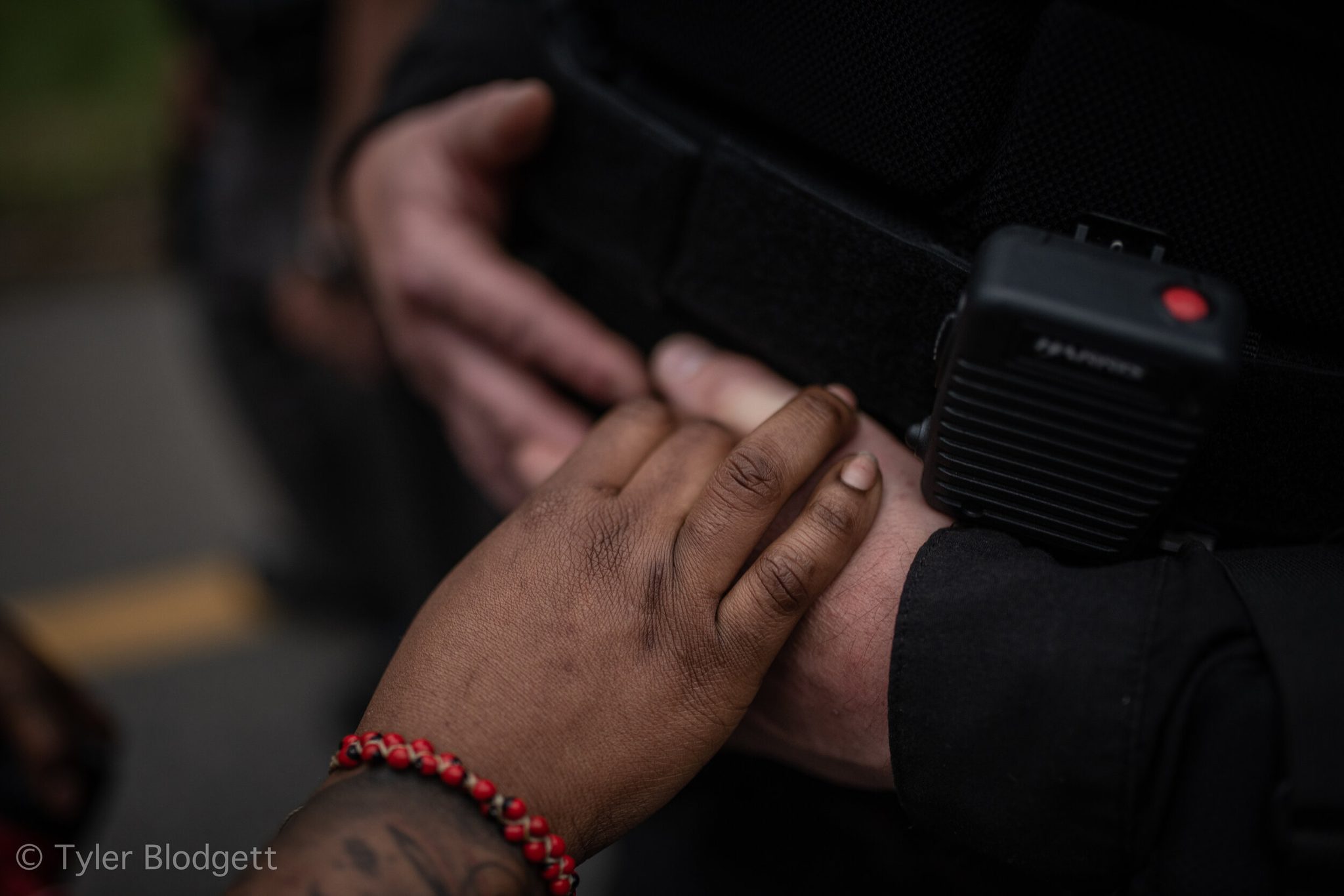 Two hands meet between a red bead bracelet and an officer's radio.