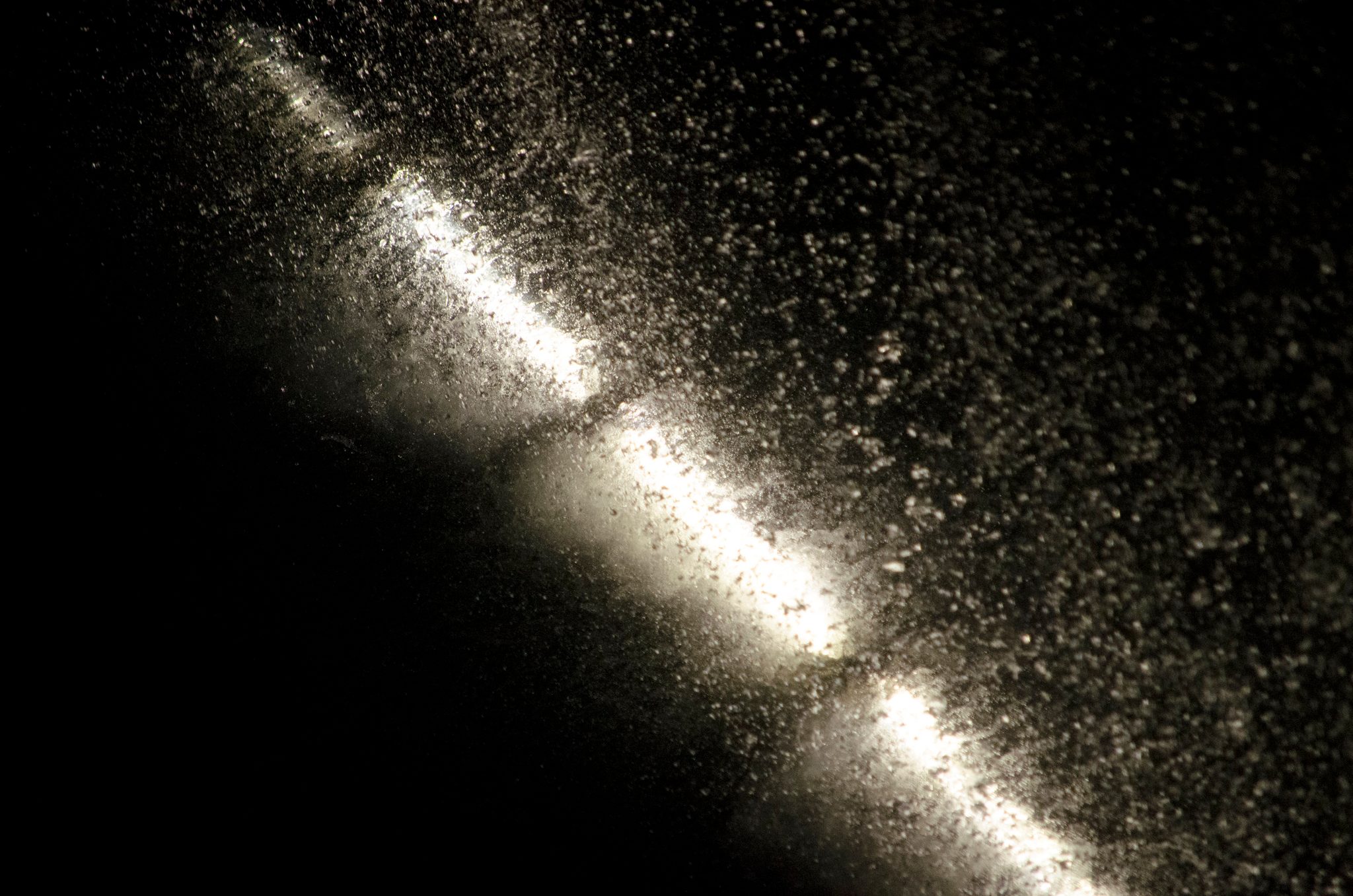 Light cuts a diagonal through a cloud of spray in the dark.