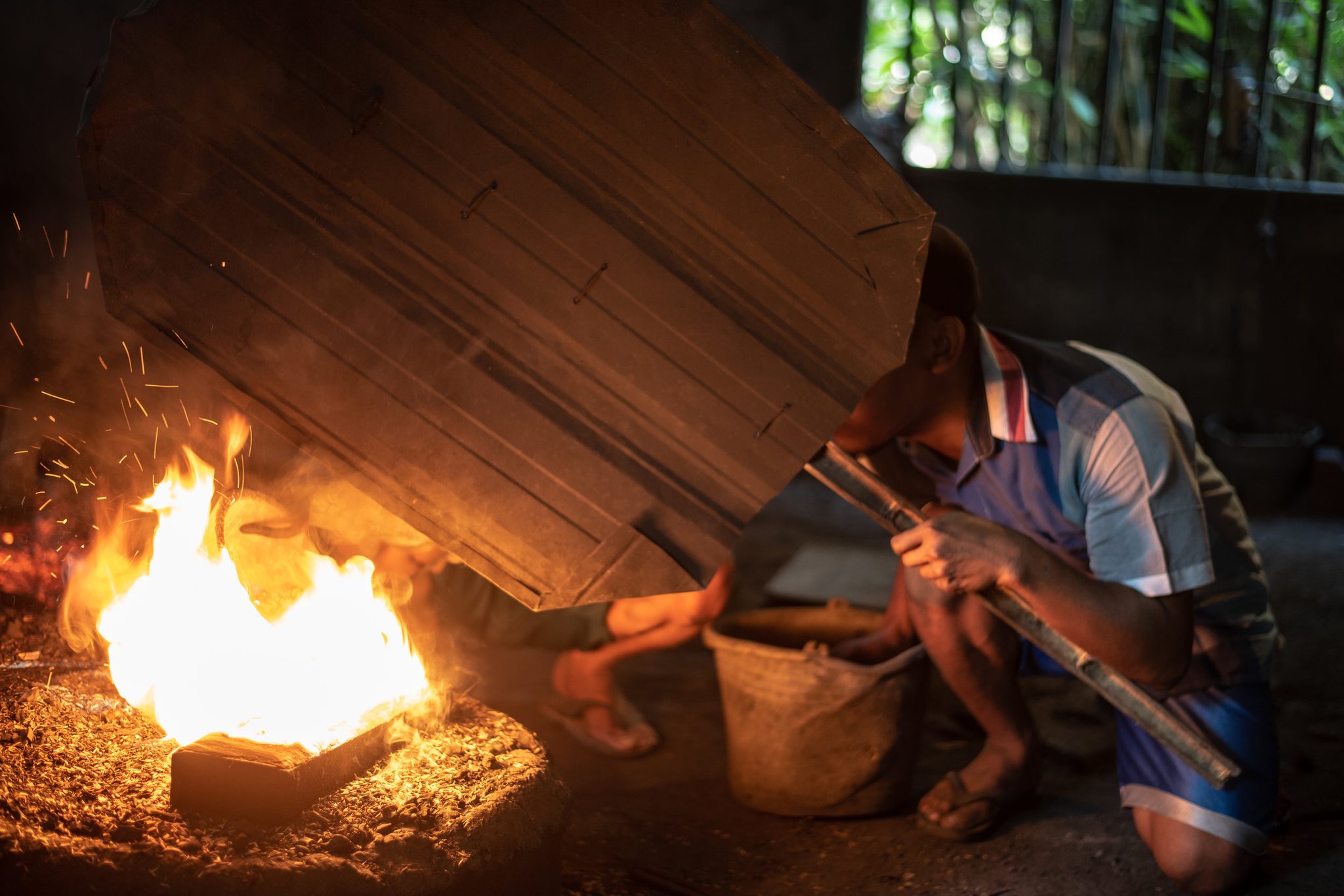 A worker shields himself behind a wooden board as the forge flares beside him.