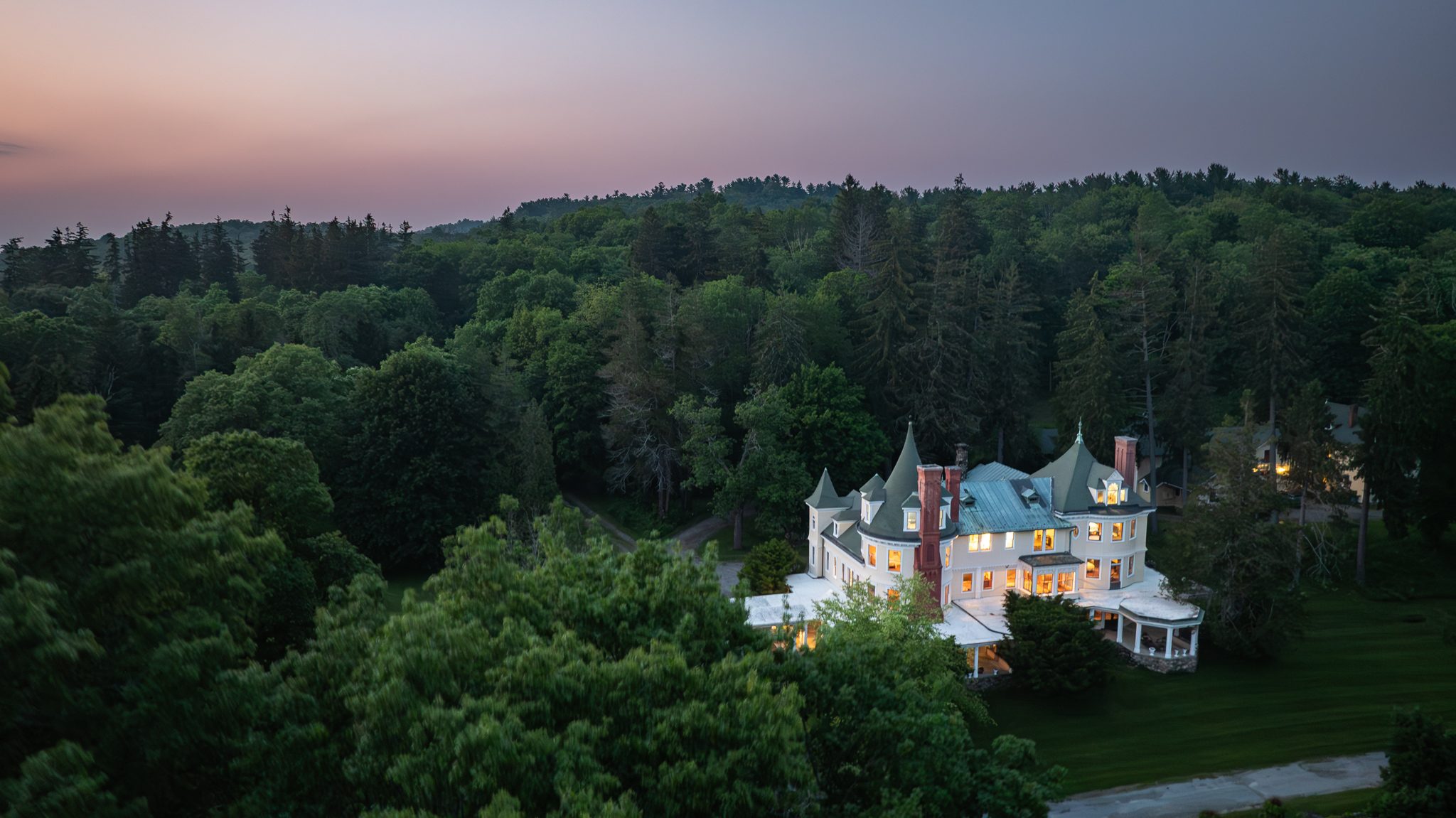 From high above at nightfall, the lit house is a small bright island in miles of dark woods.