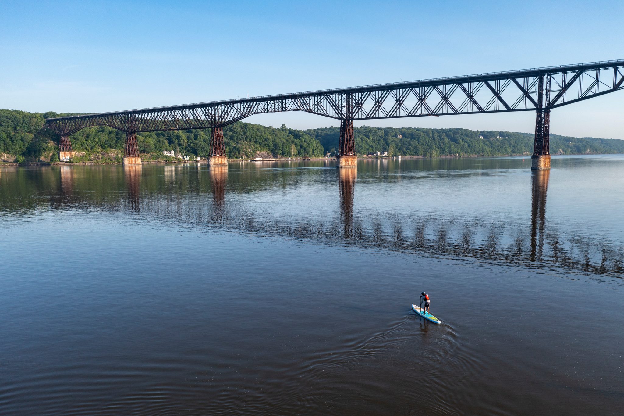 From the air, a tiny board beneath the long steel trestle of a railroad bridge and its reflection.