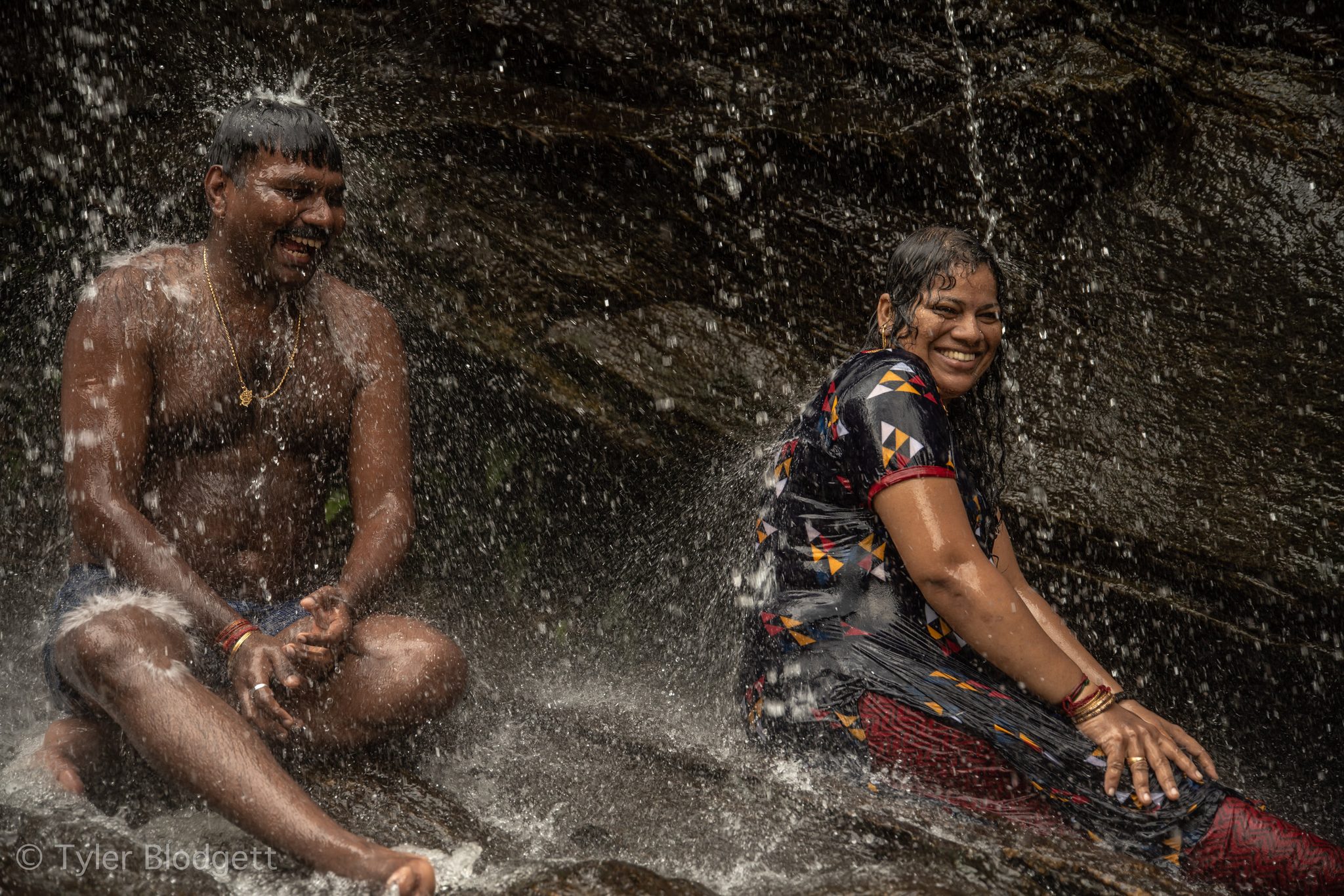 Two bathers laugh beneath the falls as the water hammers down on their shoulders.