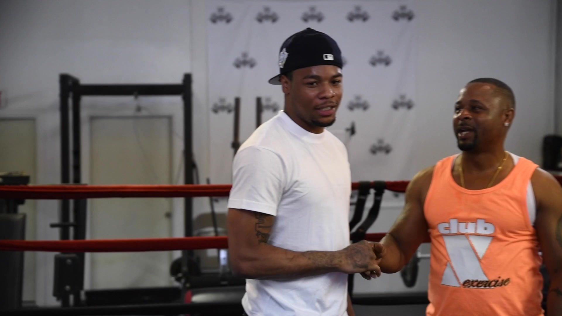 A handshake by the ring between a man in a white tee and a man in an orange Club X tank.