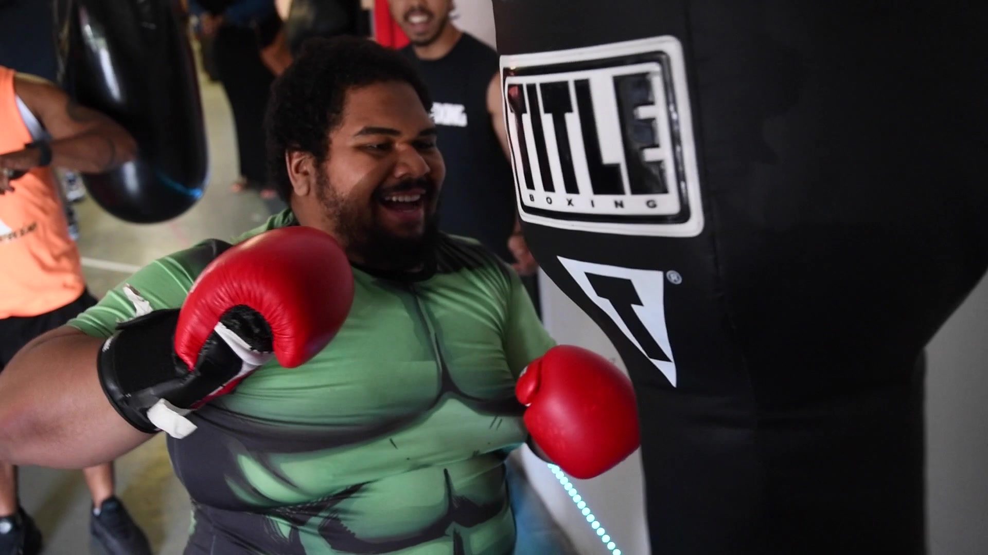 A wide grin at the heavy bag, red gloves still up while the room moves around him.