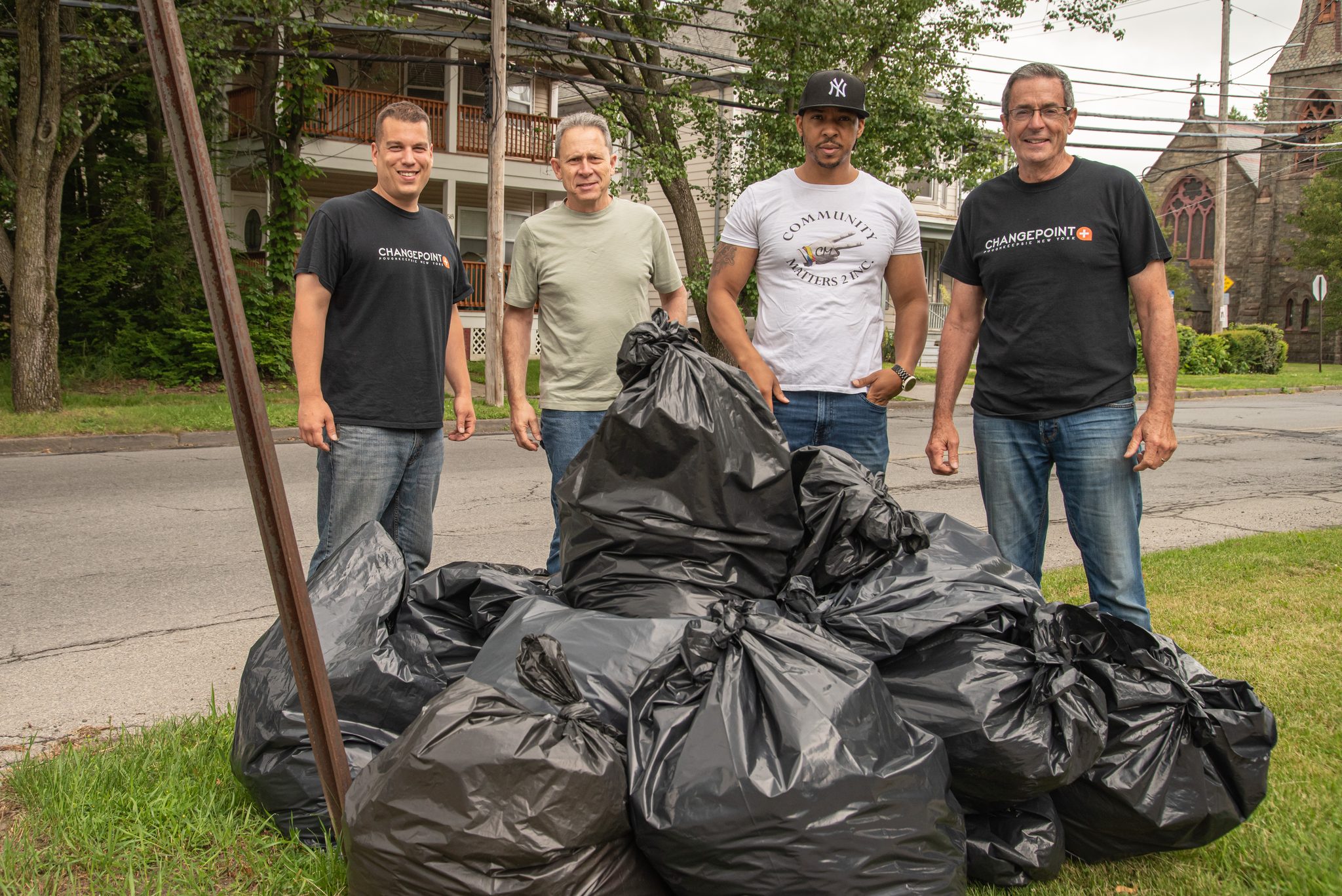 Four volunteers stand behind the morning's work, a heap of full bags at the curb.