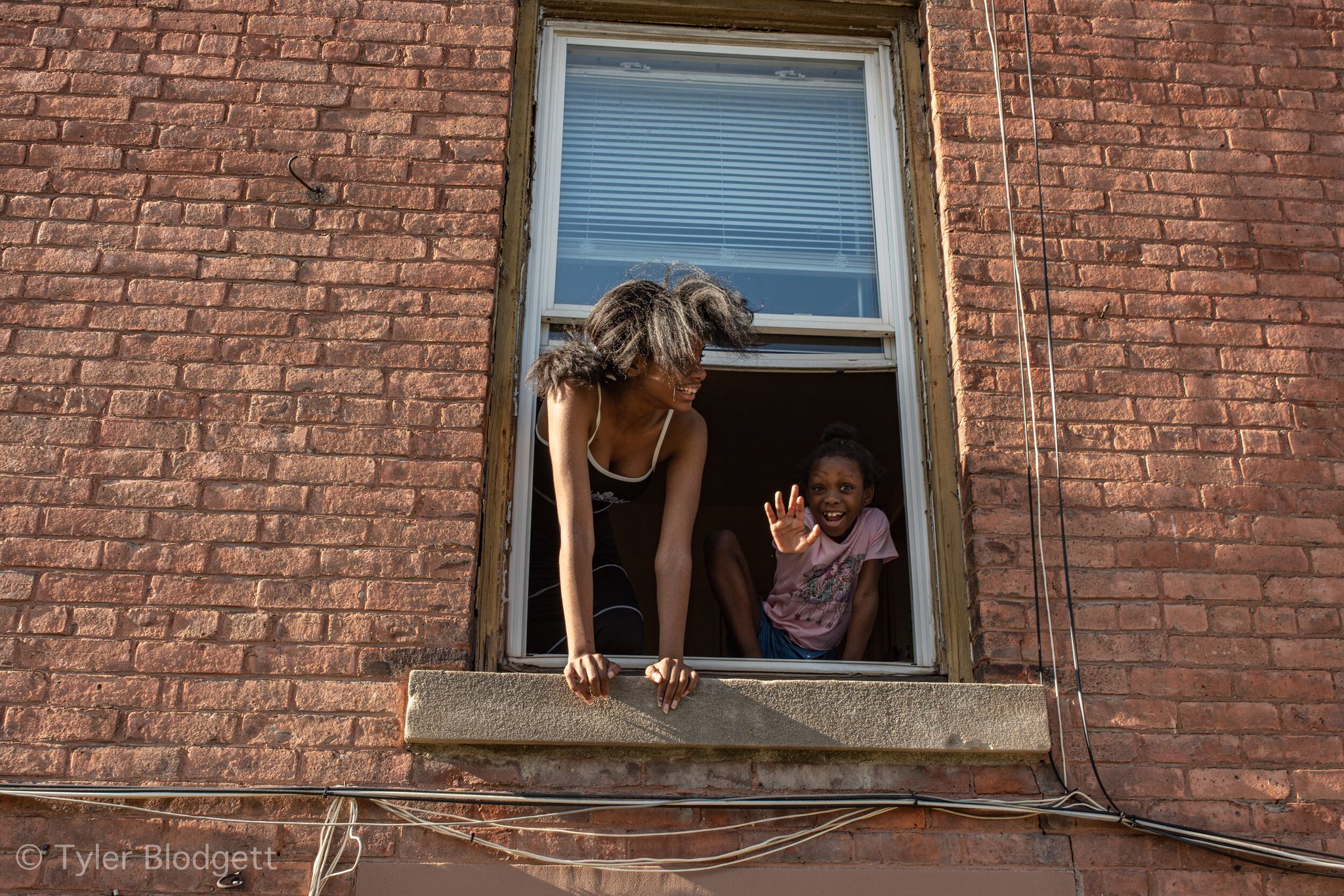 Two girls lean from a second floor window to wave at the march below.