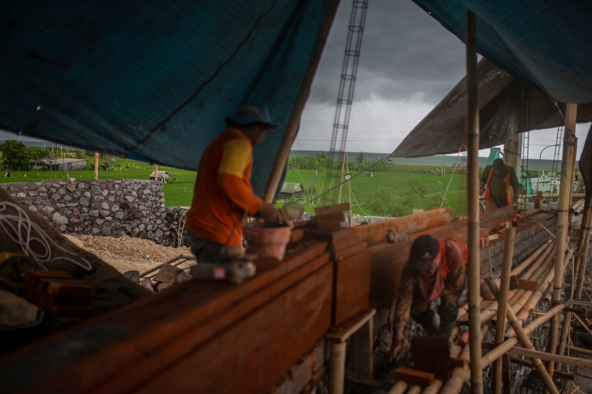 Under a blue tarp, a man works at a long wooden trough stacked with fresh-cut blocks.