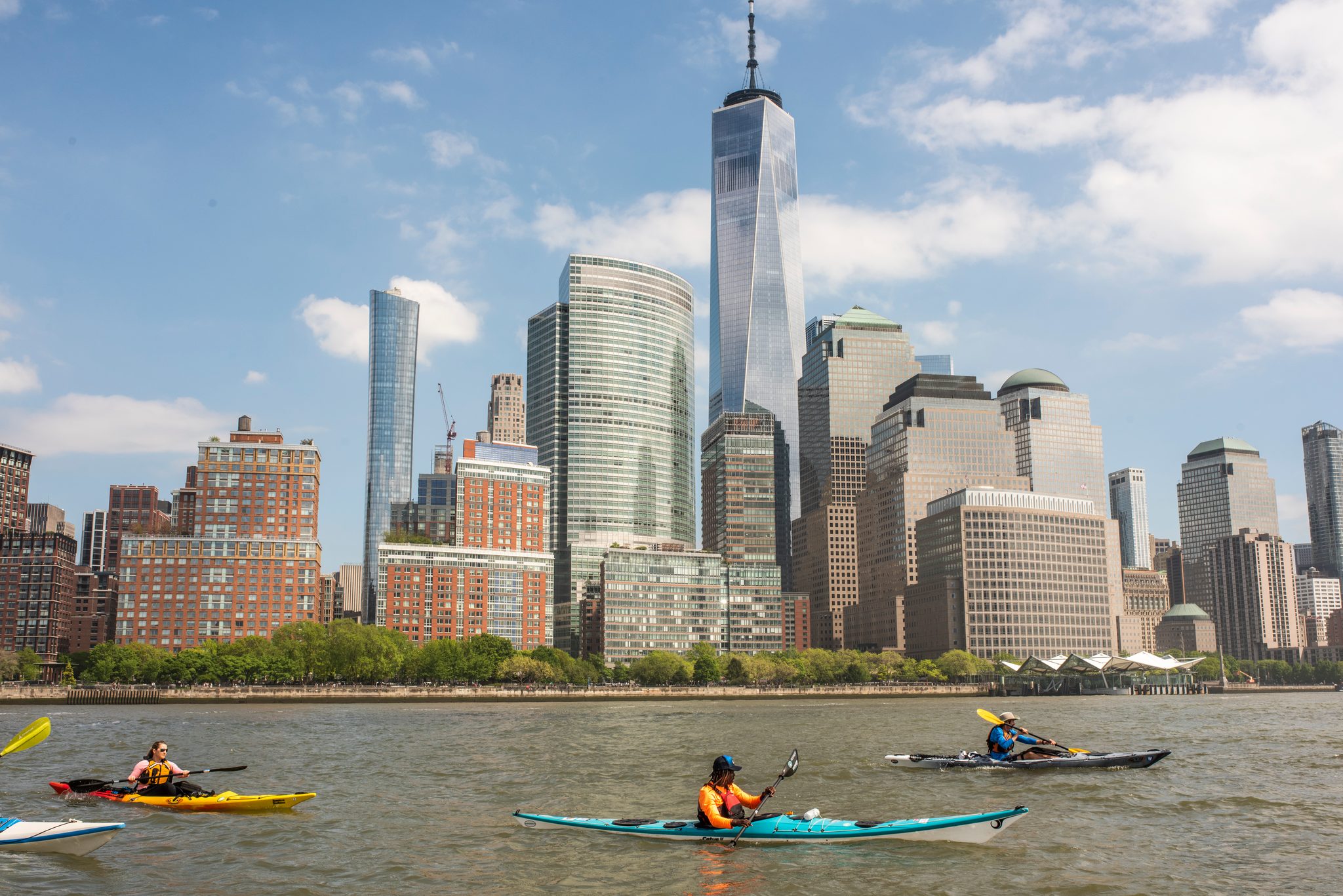 One World Trade Center rises straight up out of the frame as the paddlers cross in front of it.