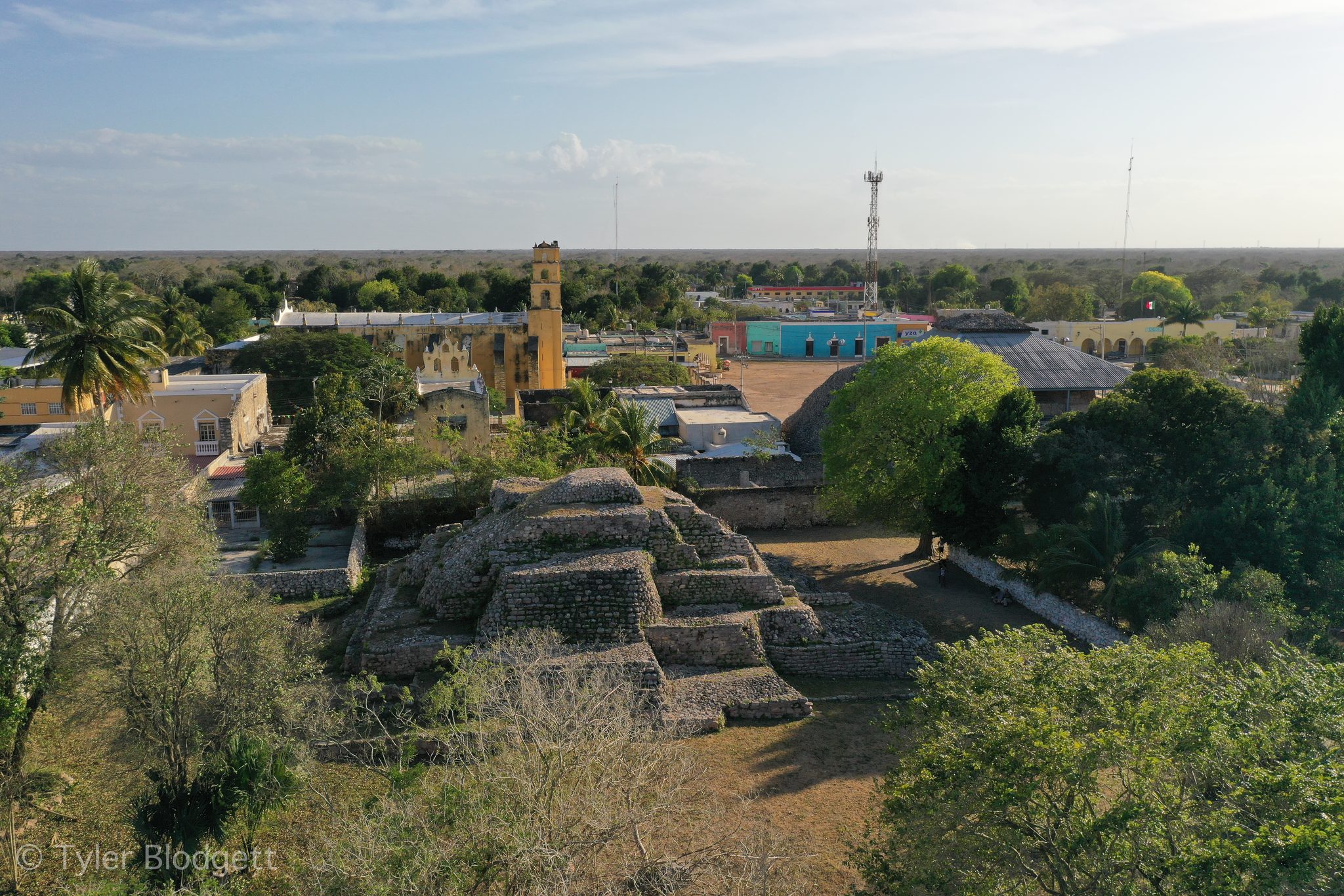 From above, the stepped ruins of a pyramid sit in the middle of town, the yellow church just beyond.