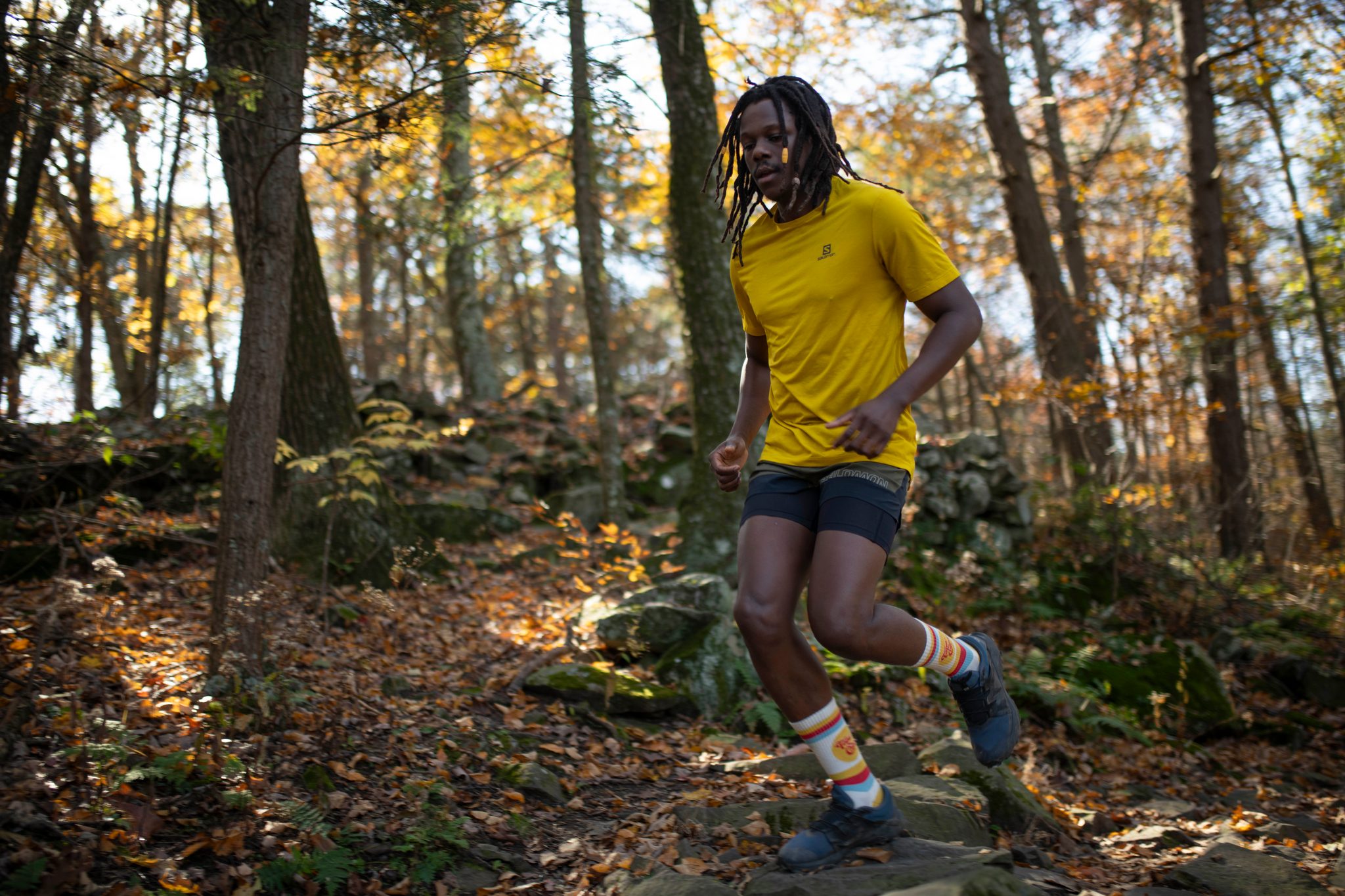 Chev runs a rocky woodland trail through yellow fall leaves, striped socks flashing.