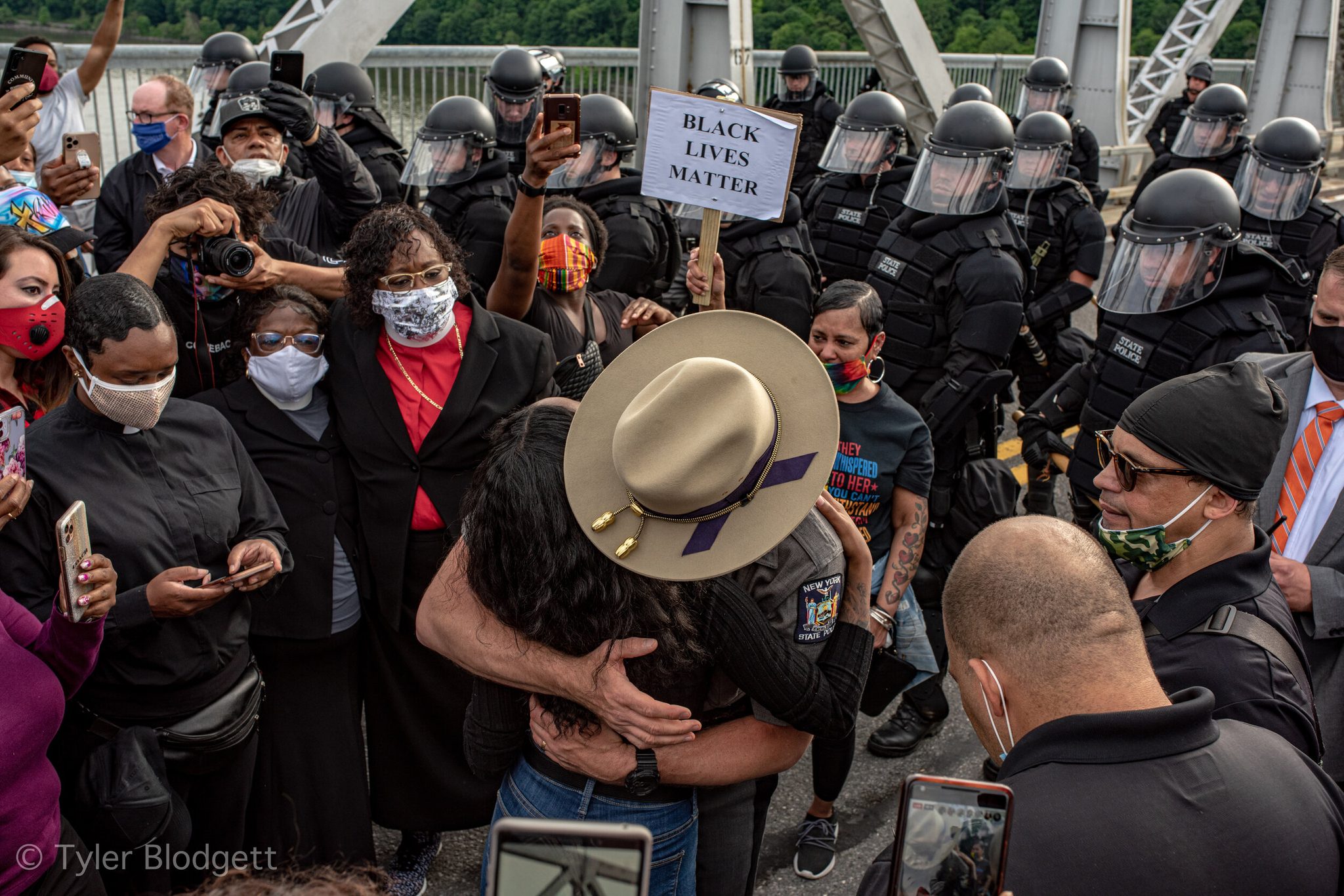 A trooper in a campaign hat pulls a marcher into a hug in front of the riot line.