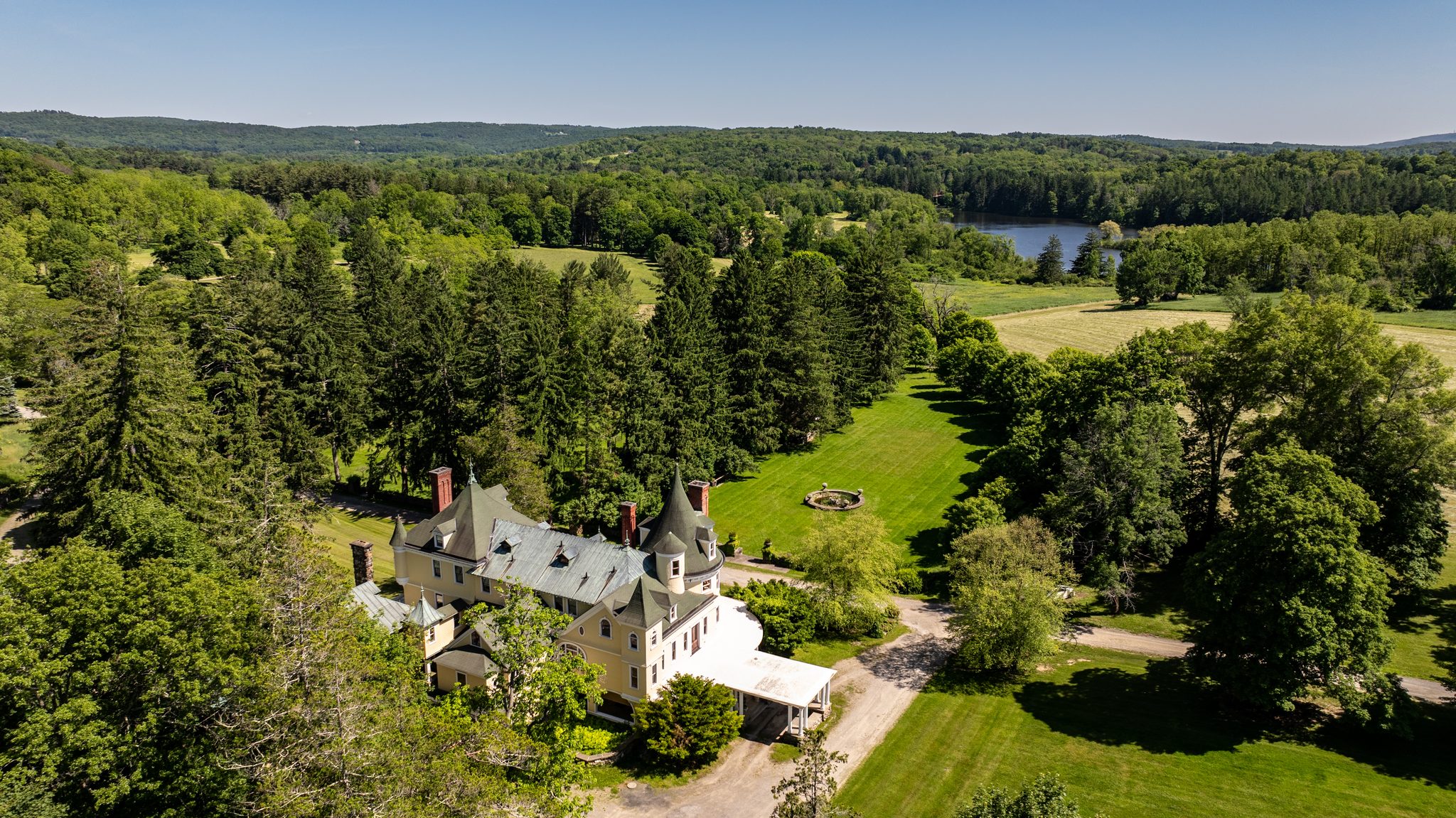 The main house seen from above, slate turrets and red chimneys sitting in a clearing of old pines and lawn.