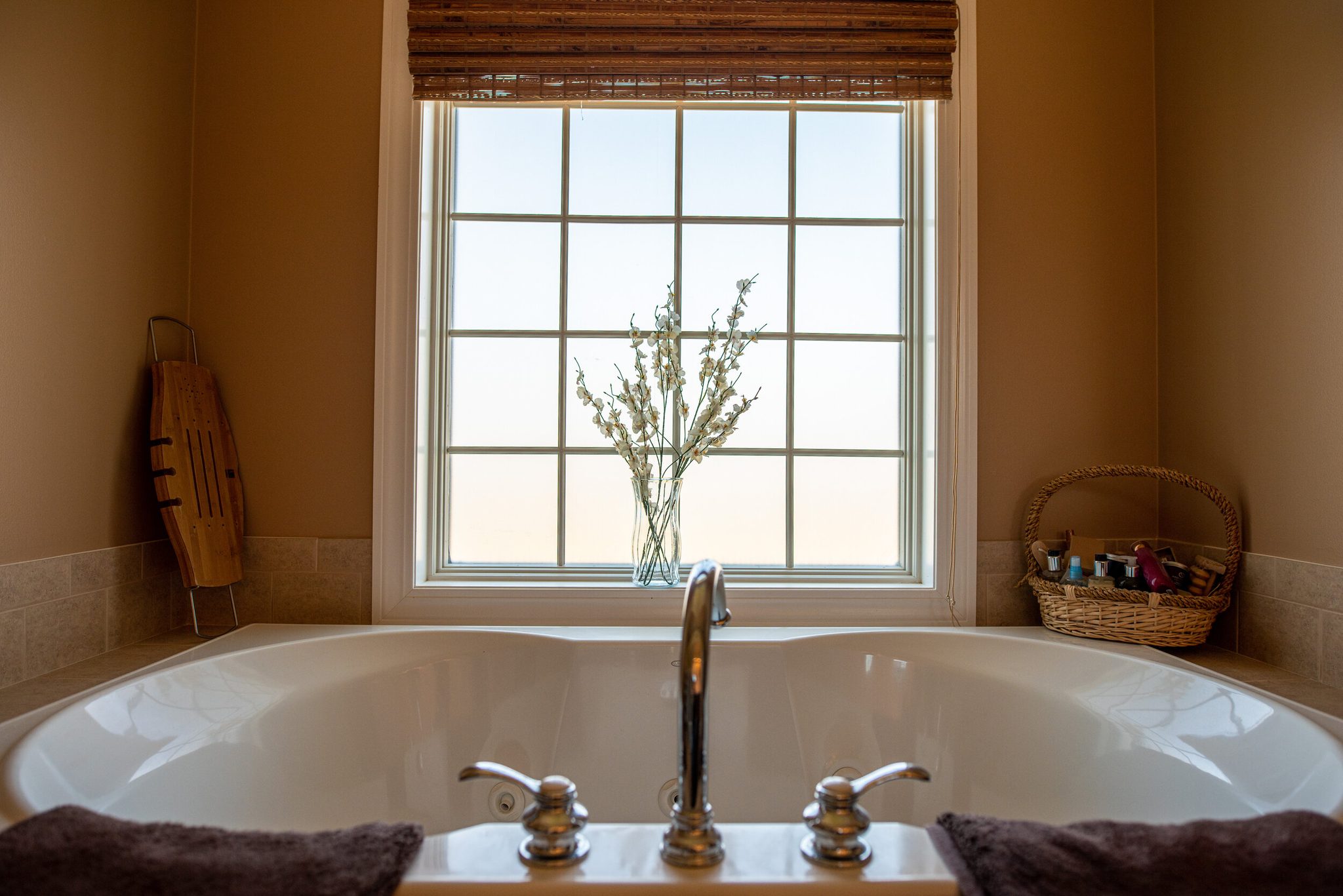 A soaking tub waits beneath a tall window, a sprig of flowers in the light.