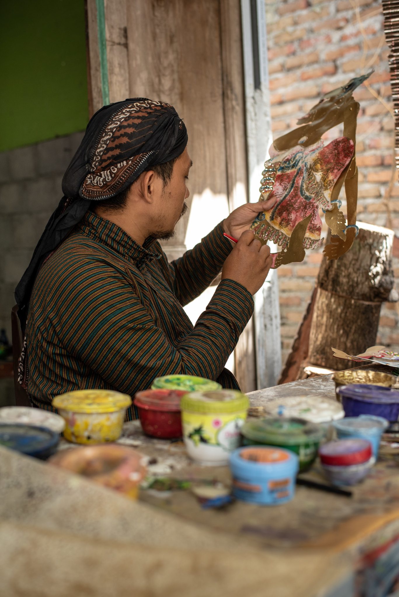 Dhidot works color into the carved leather, pots of paint crowded at his elbow.