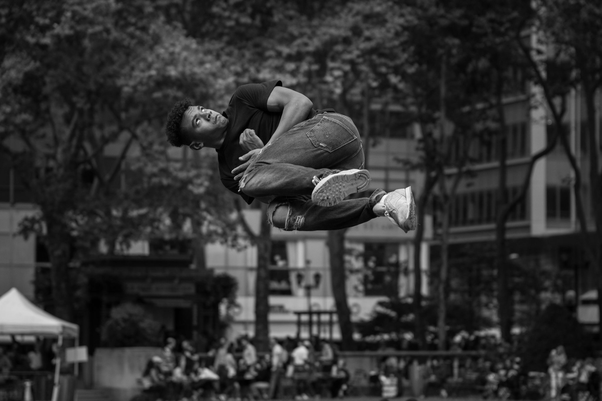 A dancer hangs in midair above the park, folded like a secret, while the crowd below barely looks up.