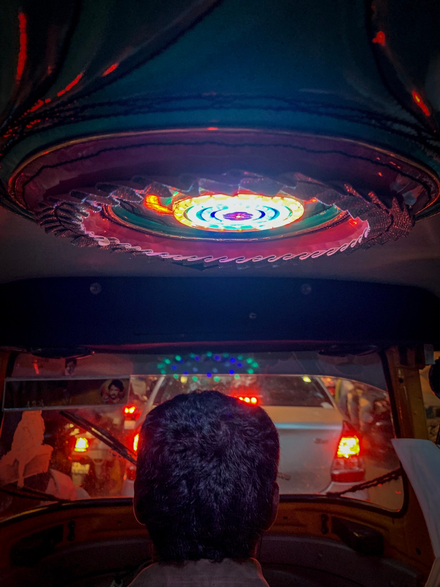 A spinning light show glows on the ceiling of an auto rickshaw at night.