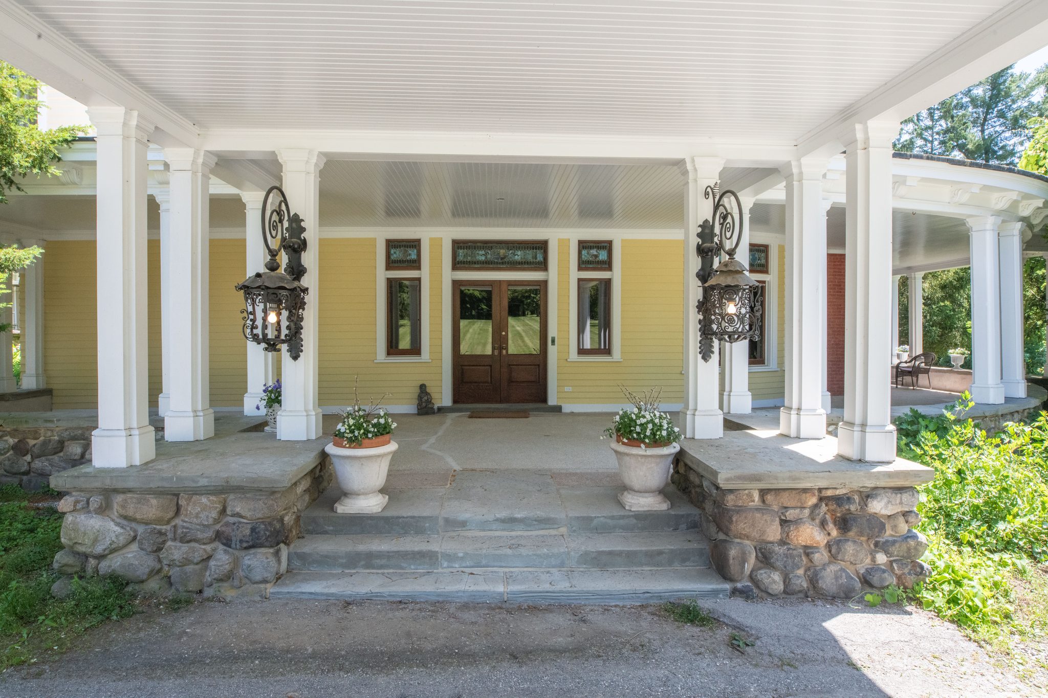 Under the porte-cochere, iron lanterns flank the double front doors, and bluestone steps sit on a base of rounded fieldstone.