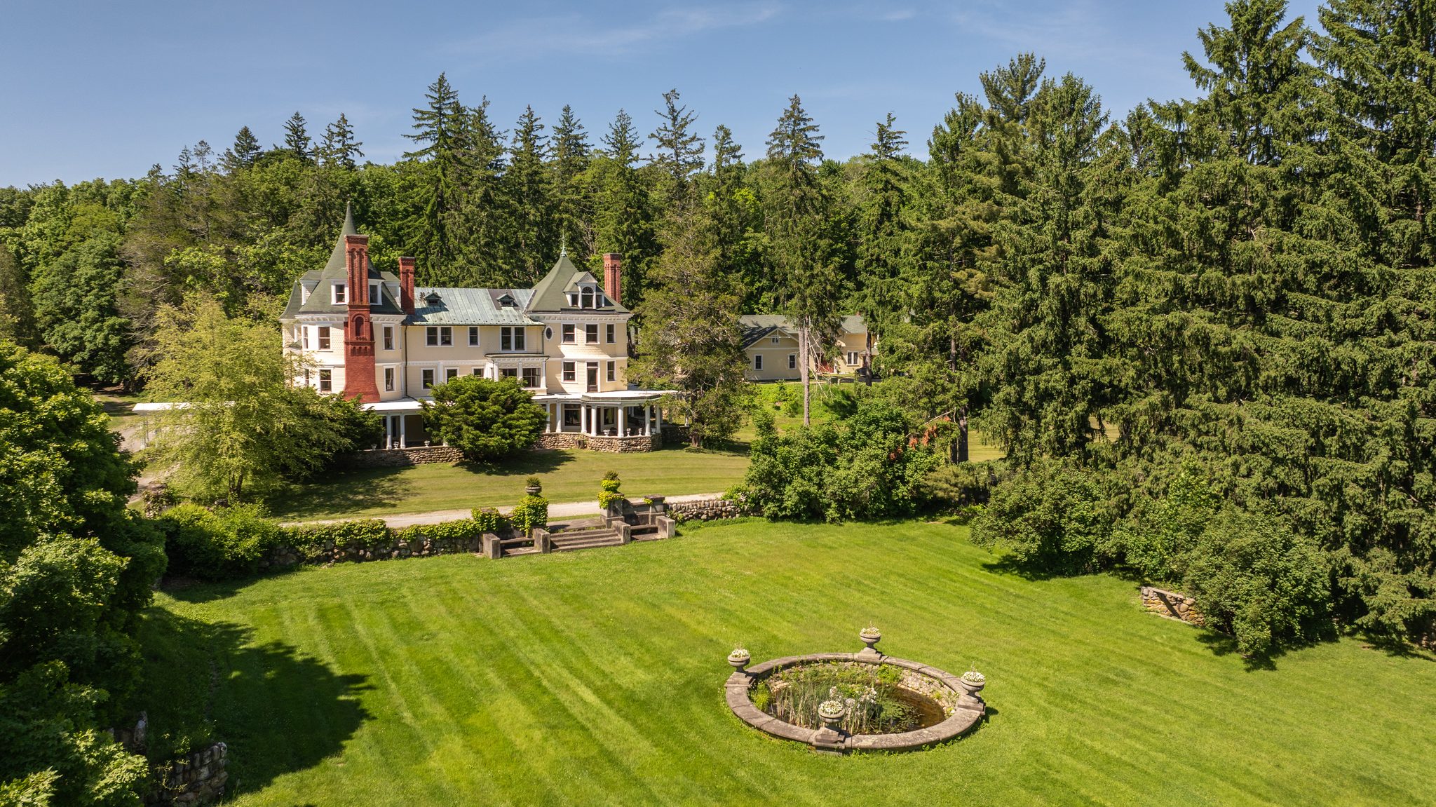 The main house, built as Daheim in the Gilded Age, looks down its long striped lawn to a round stone fountain.