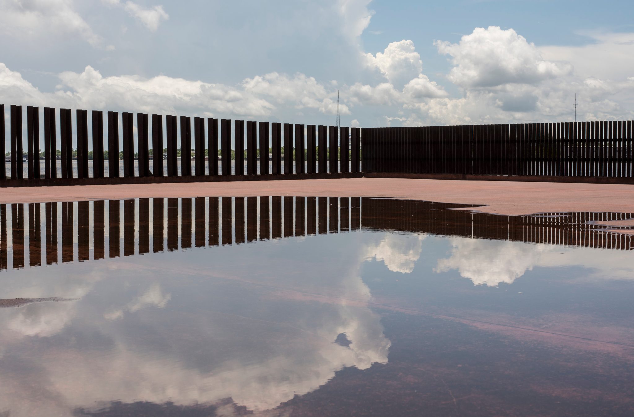 The riverfront fence stretches off in a line, the whole sky reflected at its feet.