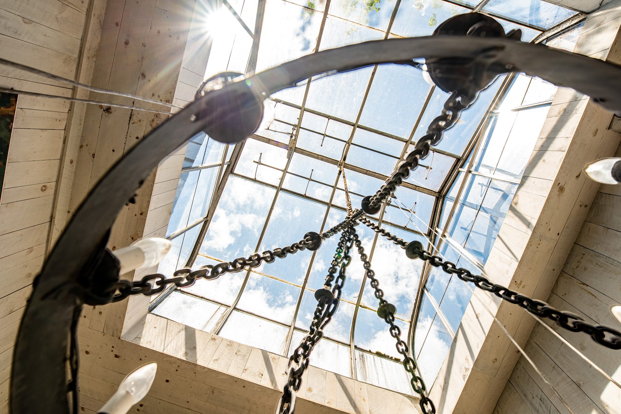 Looking straight up past the chandelier chains, a skylight opens to the summer clouds.