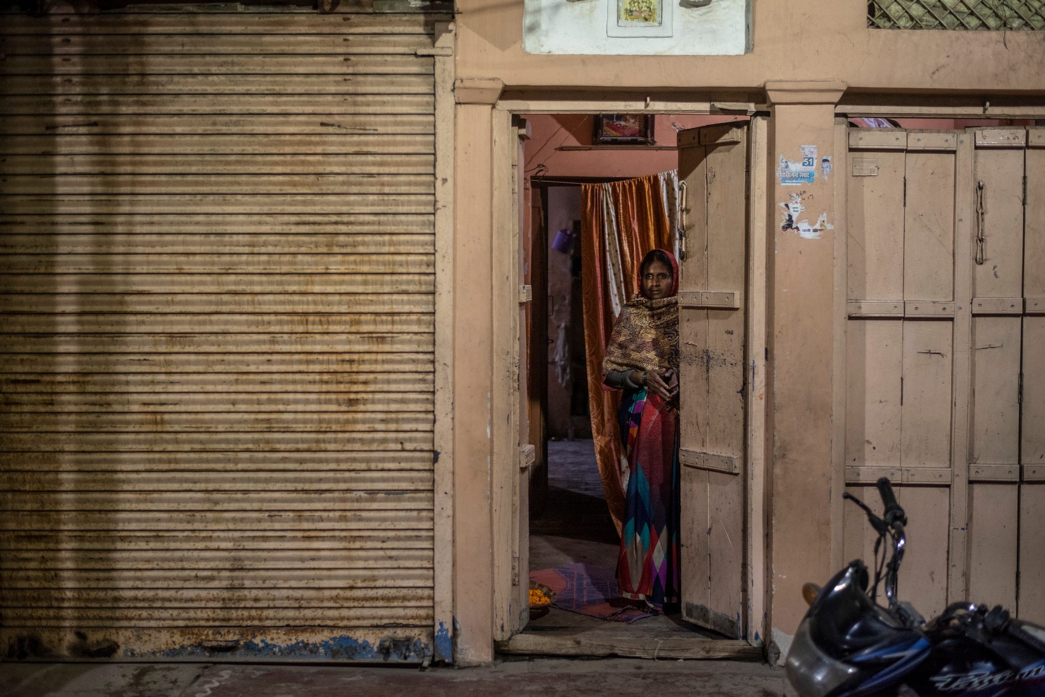 A woman watches from a lit doorway between the shuttered shops.