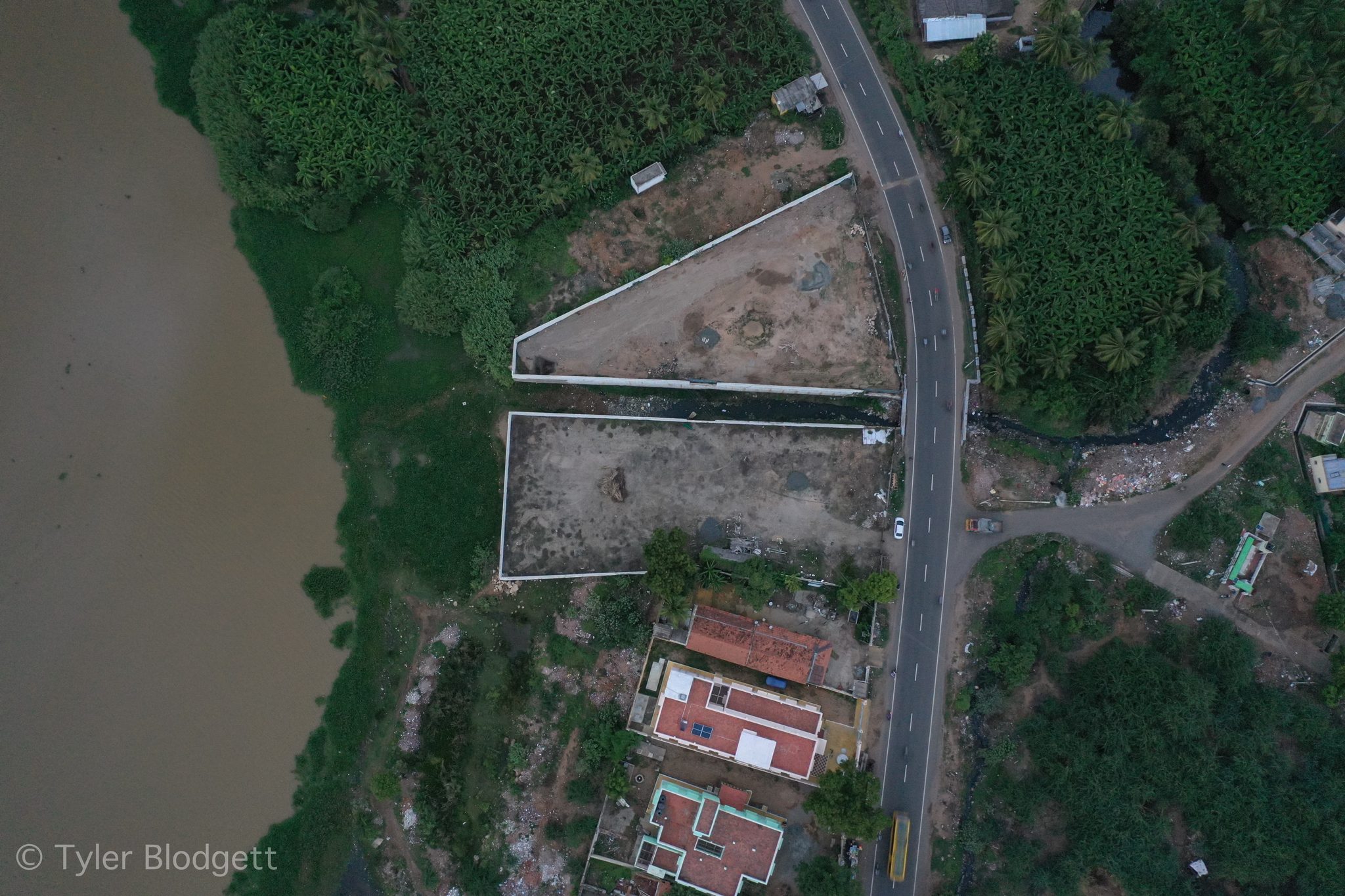 A road runs along the river past walled plots and red roofs.