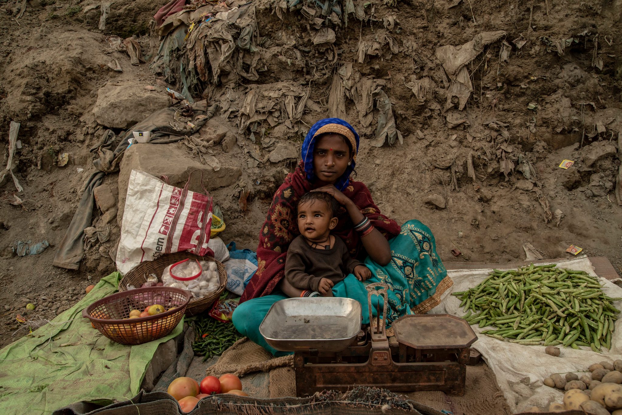 A mother sits with her toddler and sells produce roadside.