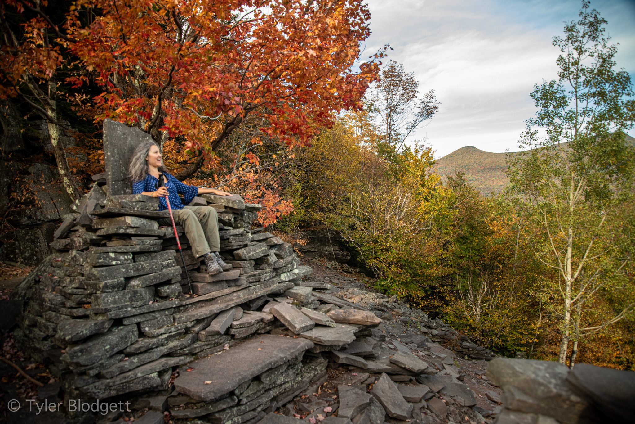 A hiker rests on a throne of stacked slate, the maples burning red around her.