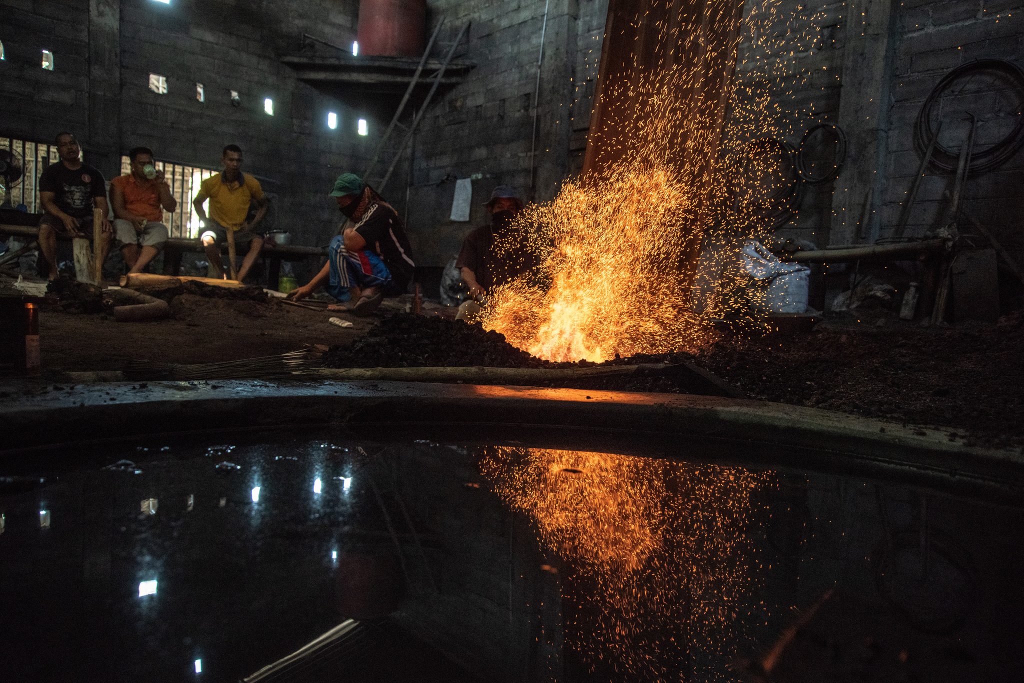 The forge's sparks double in the dark water of the cooling pool.