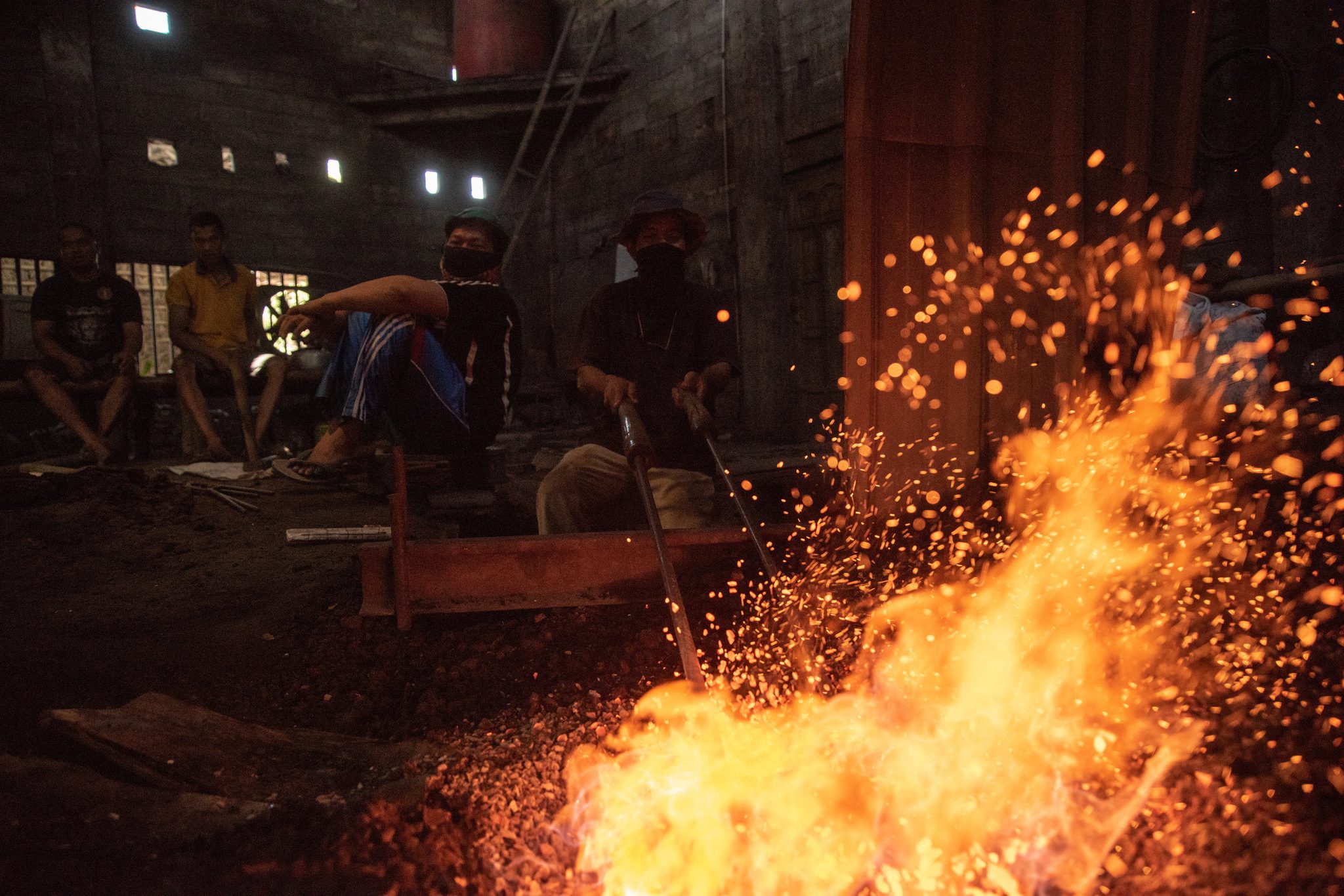 Flames and sparks rise in front of the men waiting with their tongs.