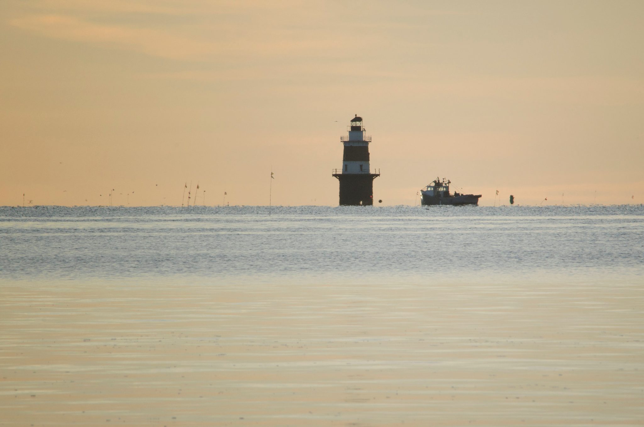 A lighthouse stands out on the Sound as a boat trawls past it.