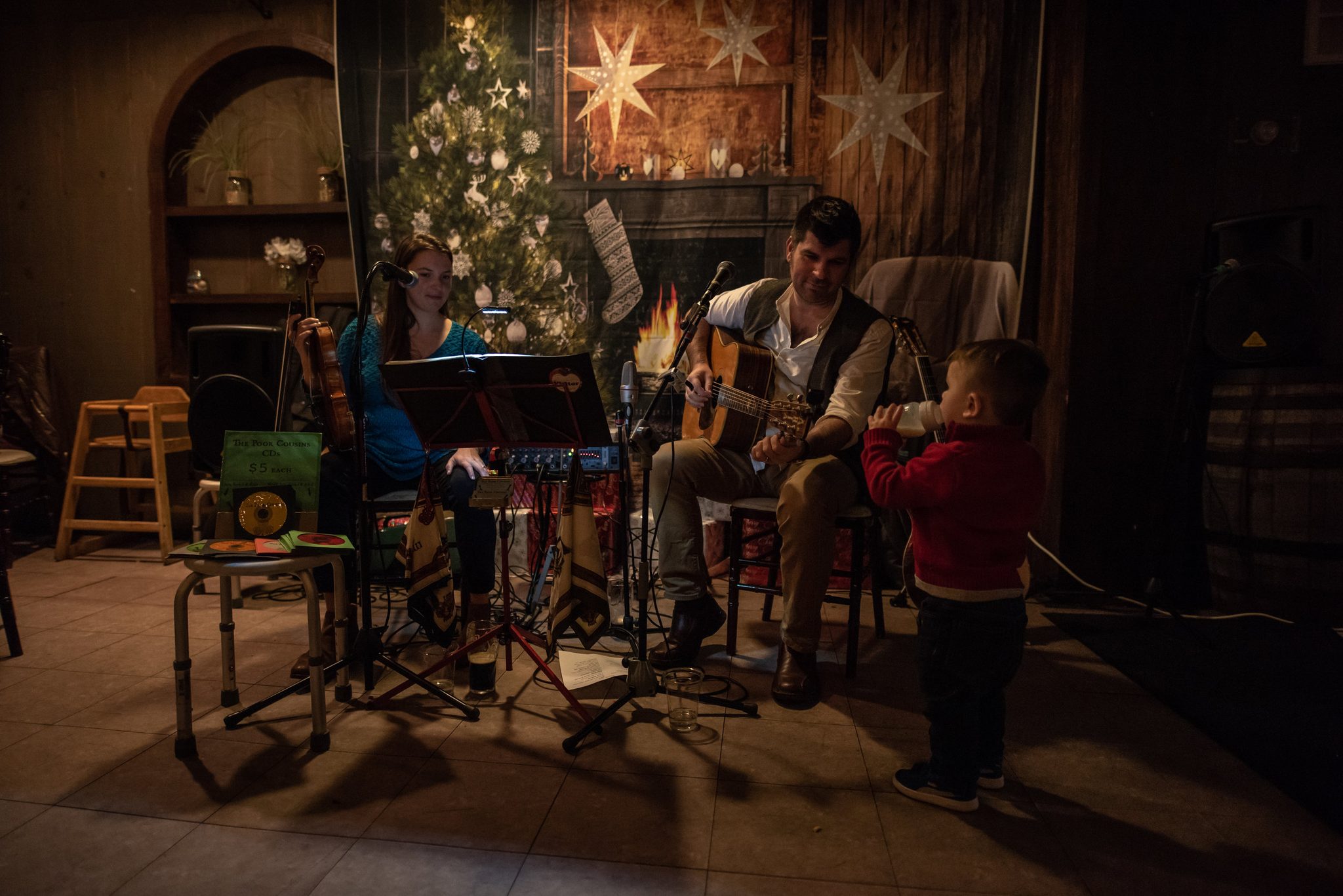 By the tree and the fire, the duo plays the holiday dinner while Ronin, bottle in hand, supervises.