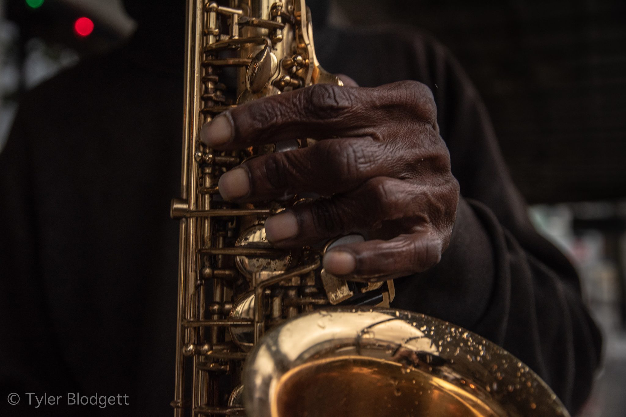 Weathered fingers on the keys of a gold saxophone.
