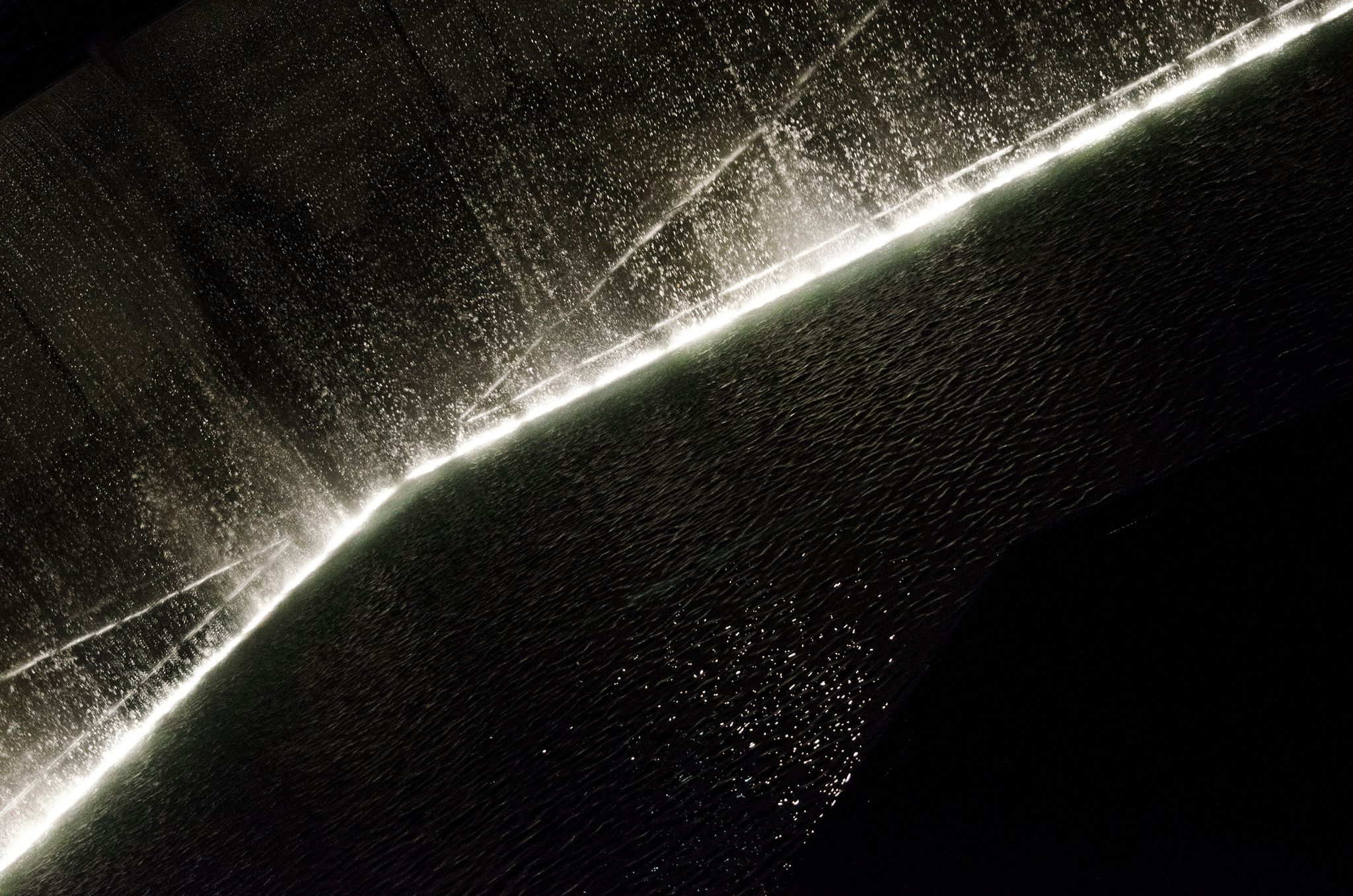 A line of light slashes across falling water in the dark.