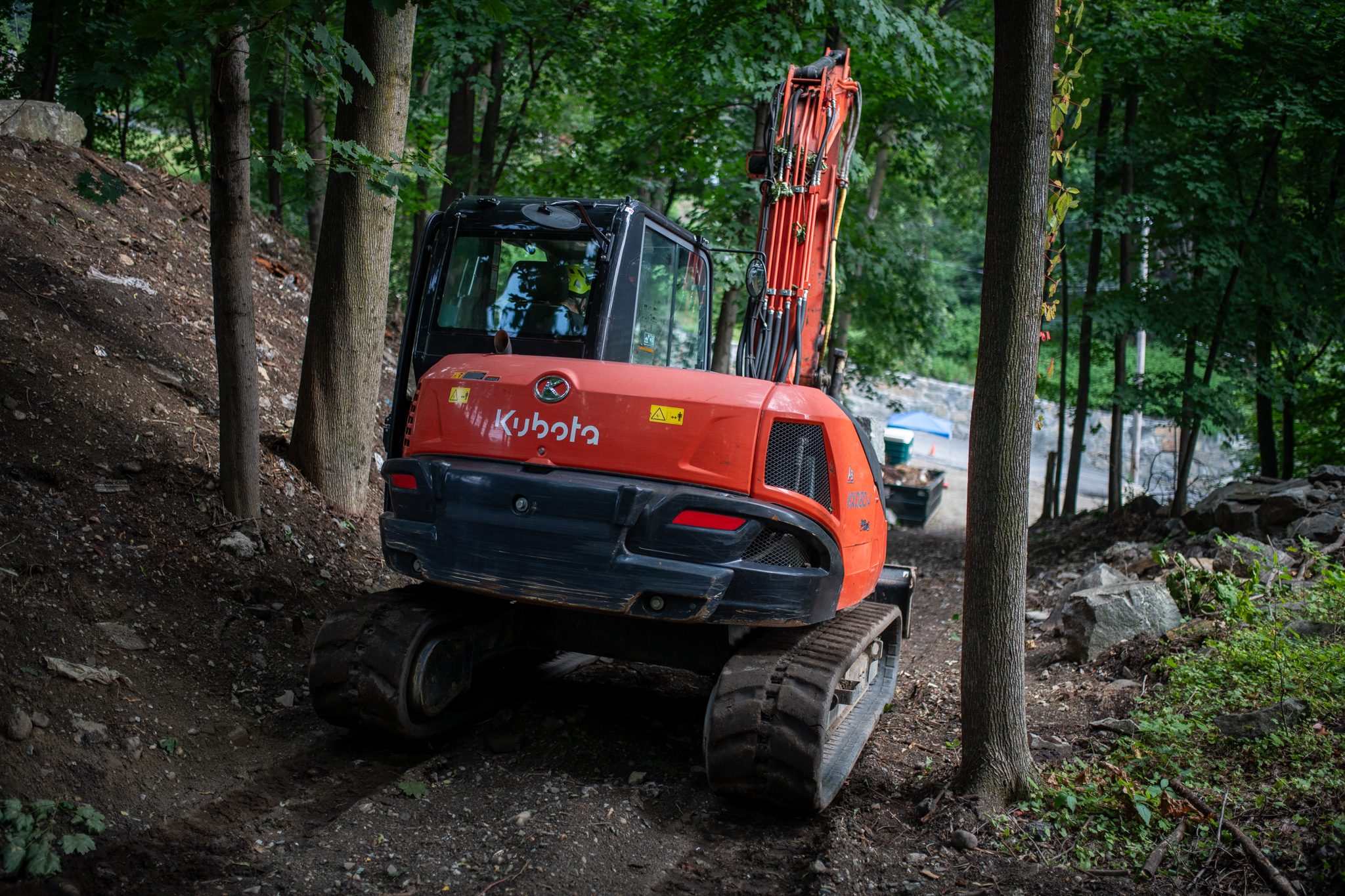 The orange excavator crawls up the new trail through the trees.