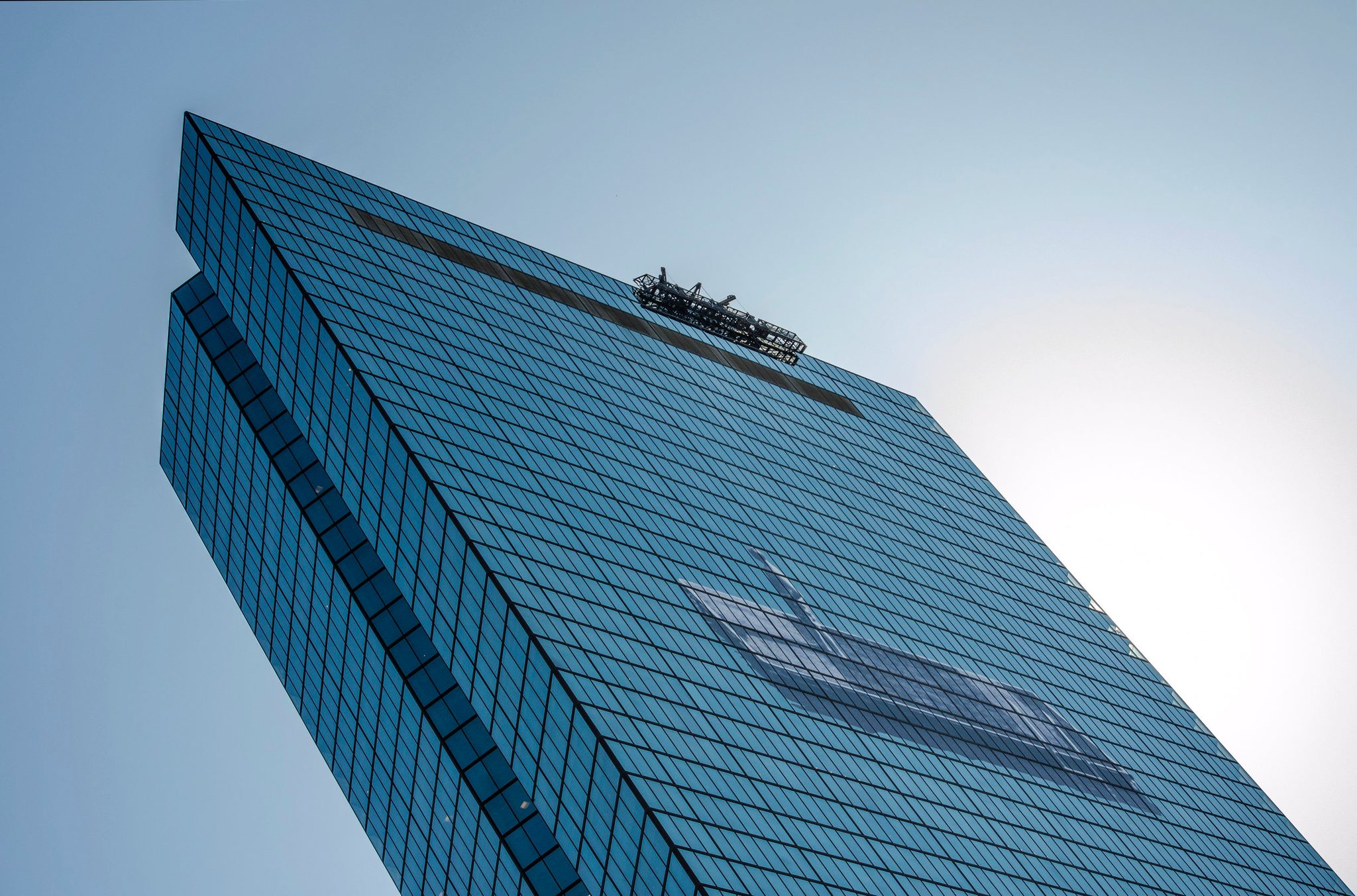 A blue glass tower leans against the sky, seen from its foot.