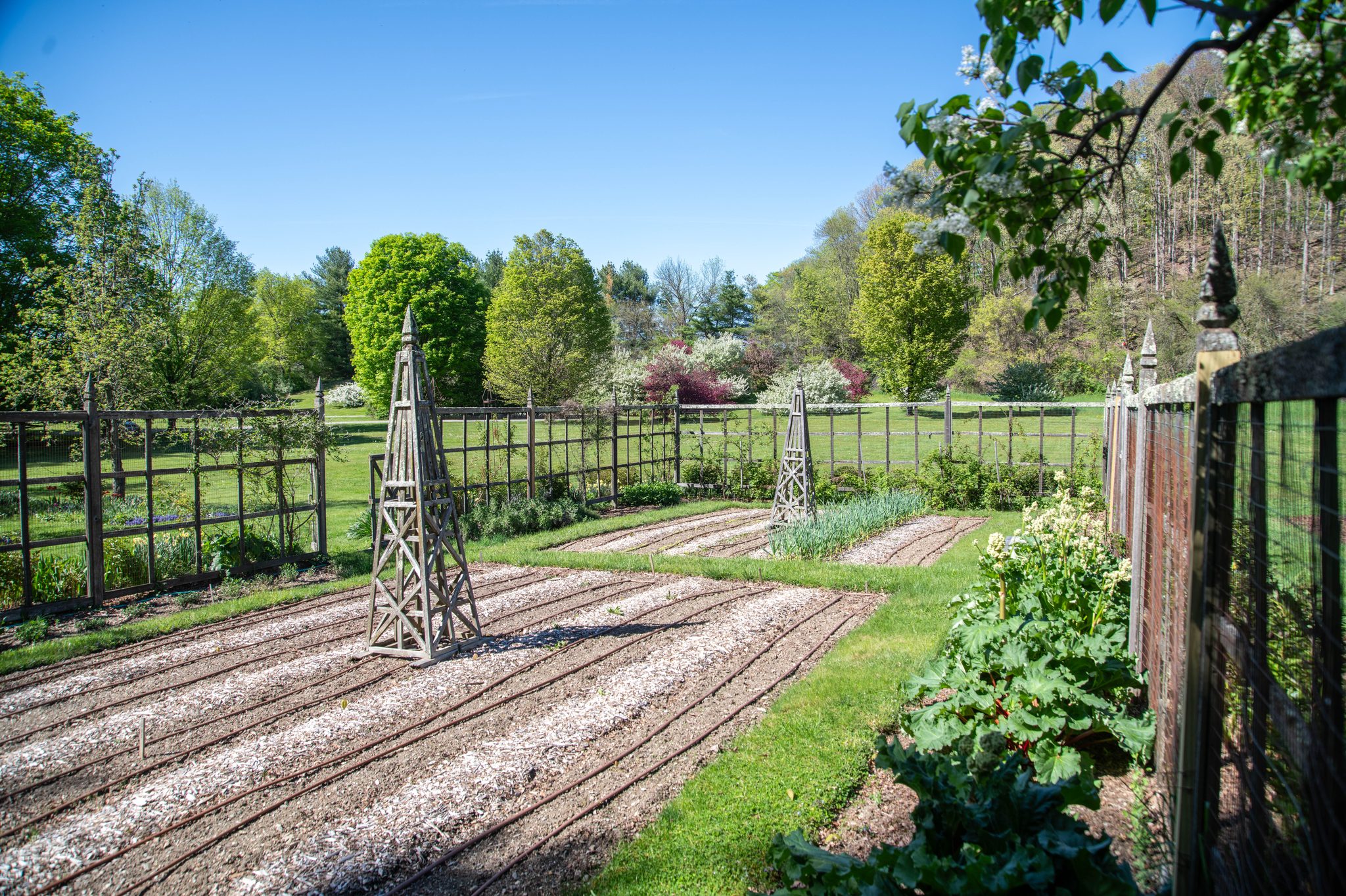 The kitchen garden in early May, beds raked and waiting, the wooden obelisks already standing guard.