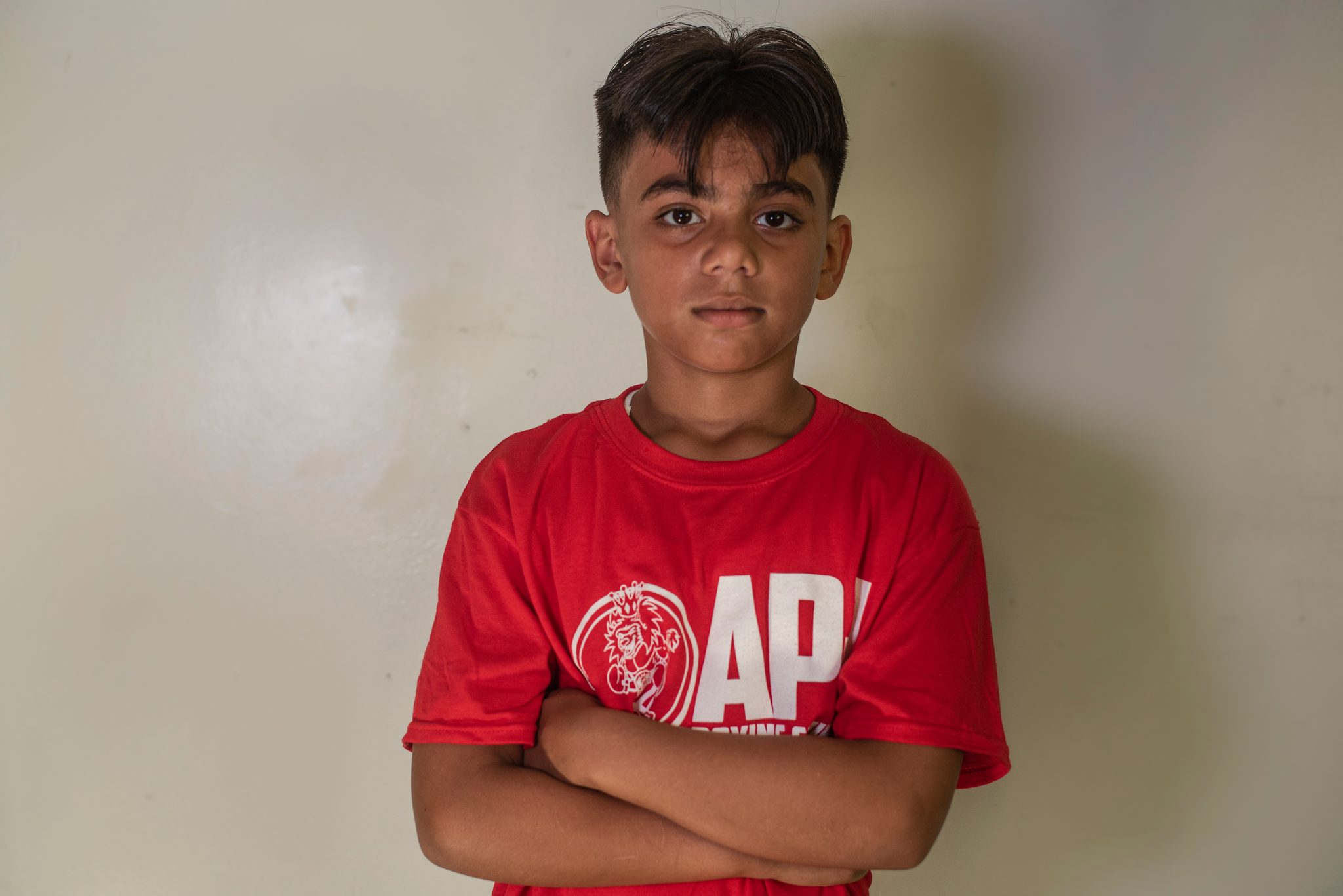 Arms folded against the white wall, sizing up the camera.