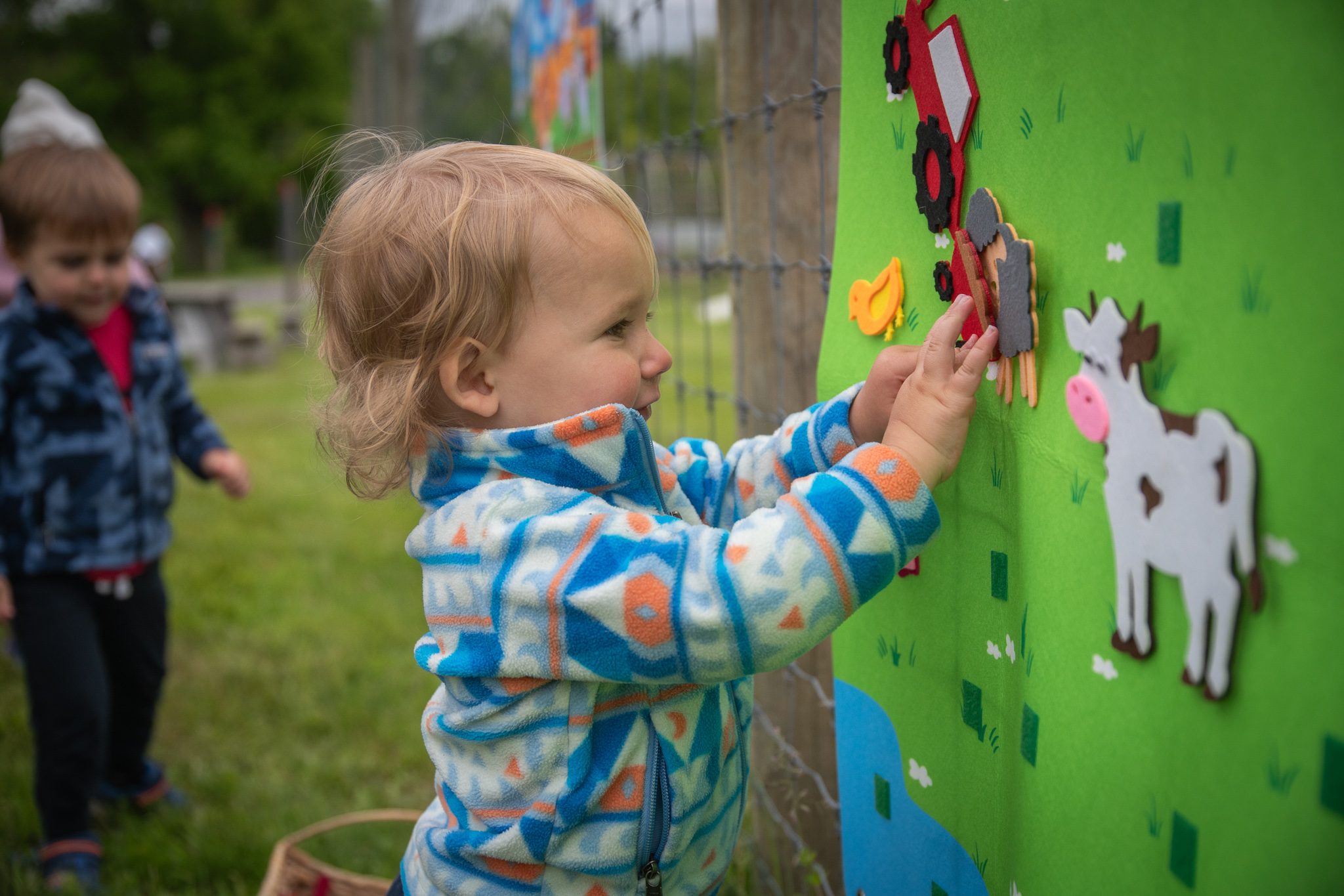 A toddler presses a felt tractor onto the farm board, a felt cow already in place.