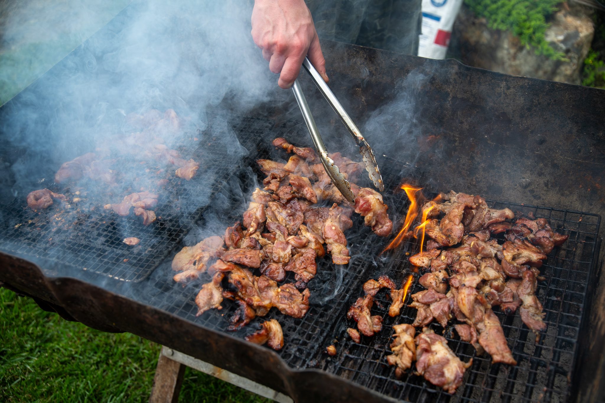 Flames lick the meat on the grill as the tongs go to work.