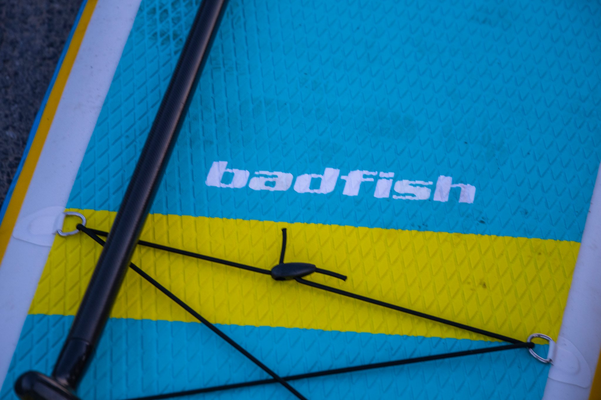 Deck pad and paddle shaft, the board's bright blue and yellow waiting on the asphalt.