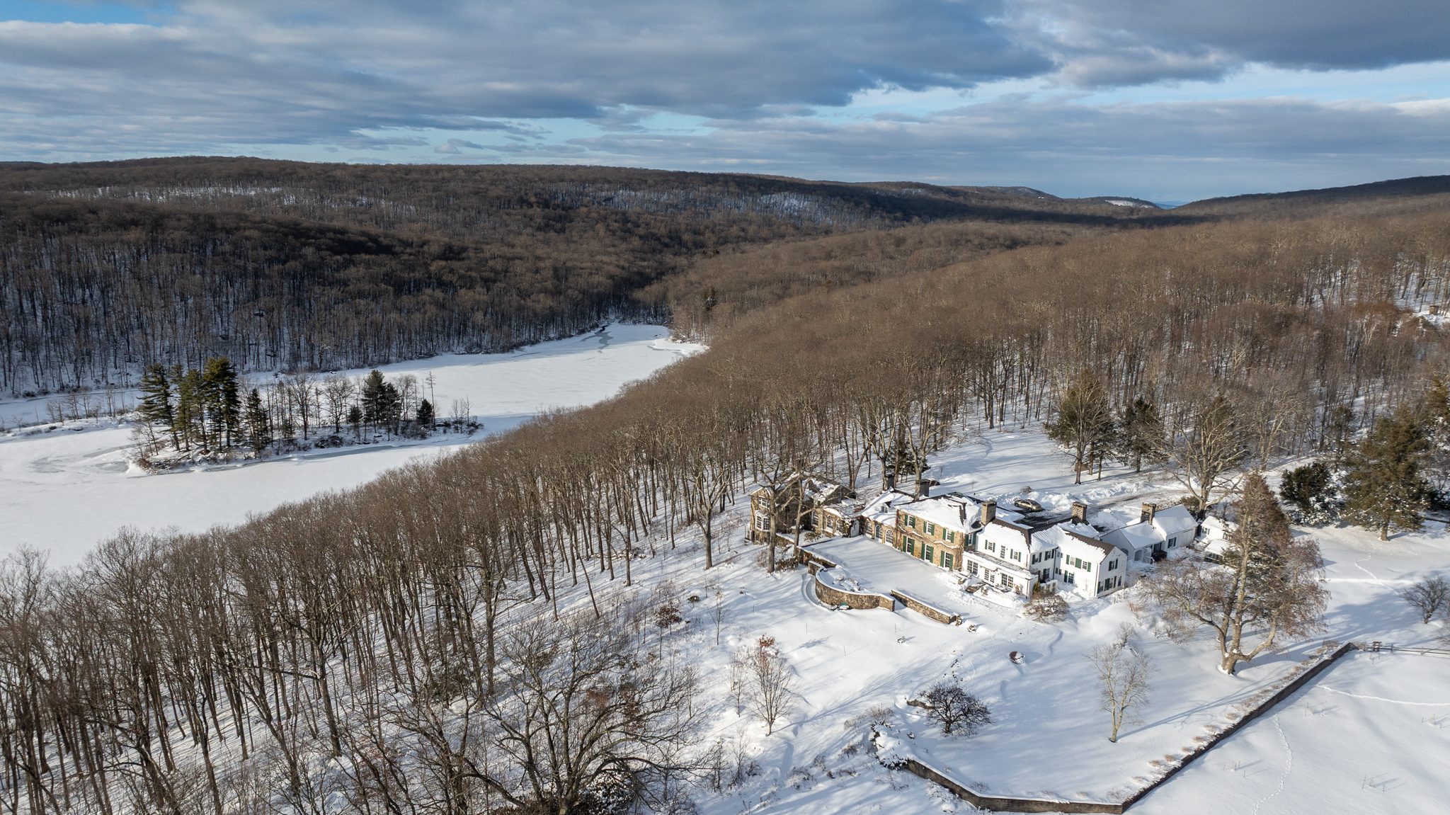 The estate sits at the edge of a frozen lake, wooded ridges rolling away beyond.