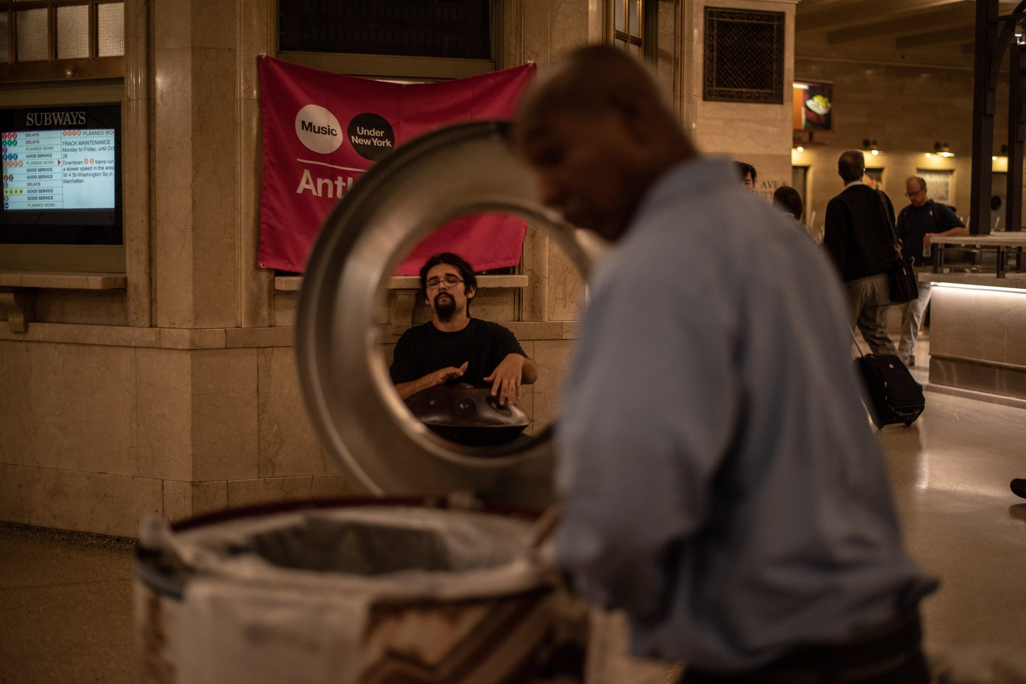 A commuter lifts the steel lid of a trash can, and Anthony appears framed inside it.